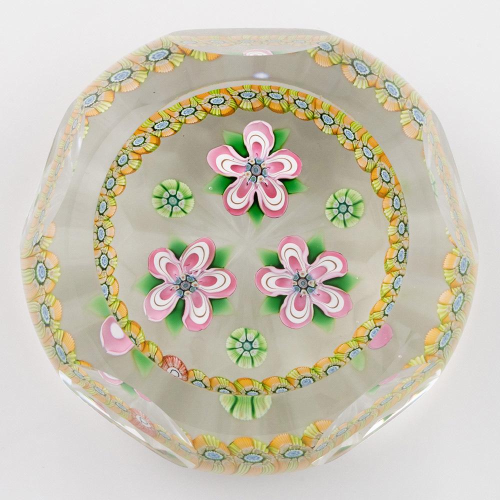 Titolo : Primule sfaccettate del Perthshire, fermacarte 1985B
Data: 1985
Origine : Scozia
Caratteristiche :Tre fiori bianchi e rosa, tre canne distanziate con una ghirlanda millefiori, una sfaccettatura superiore e cinque sfaccettature