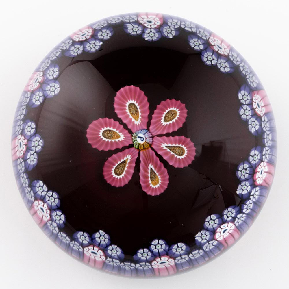 Intitulé : Presse-papier Perthshire Motif Millefiori 1977E
Date :1977
Origine : Ecosse
Caractéristiques : Six cannes en forme de pétales disposées autour d'une canne centrale pour former une fleur, entourée d'une guirlande festonnée.
Marques : P