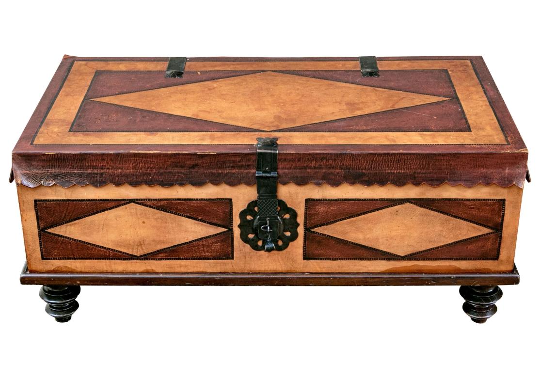 Peruanischer Trunk-Cocktailtisch aus honigfarbenem hellbraunem und dunkelrotbraunem Leder. Scharnierförmiger Deckel mit Wellenrand, der eine rechteckige Form überragt, die durchgehend mit Navette-Motiven verkleidet ist. Mit einem dekorativen