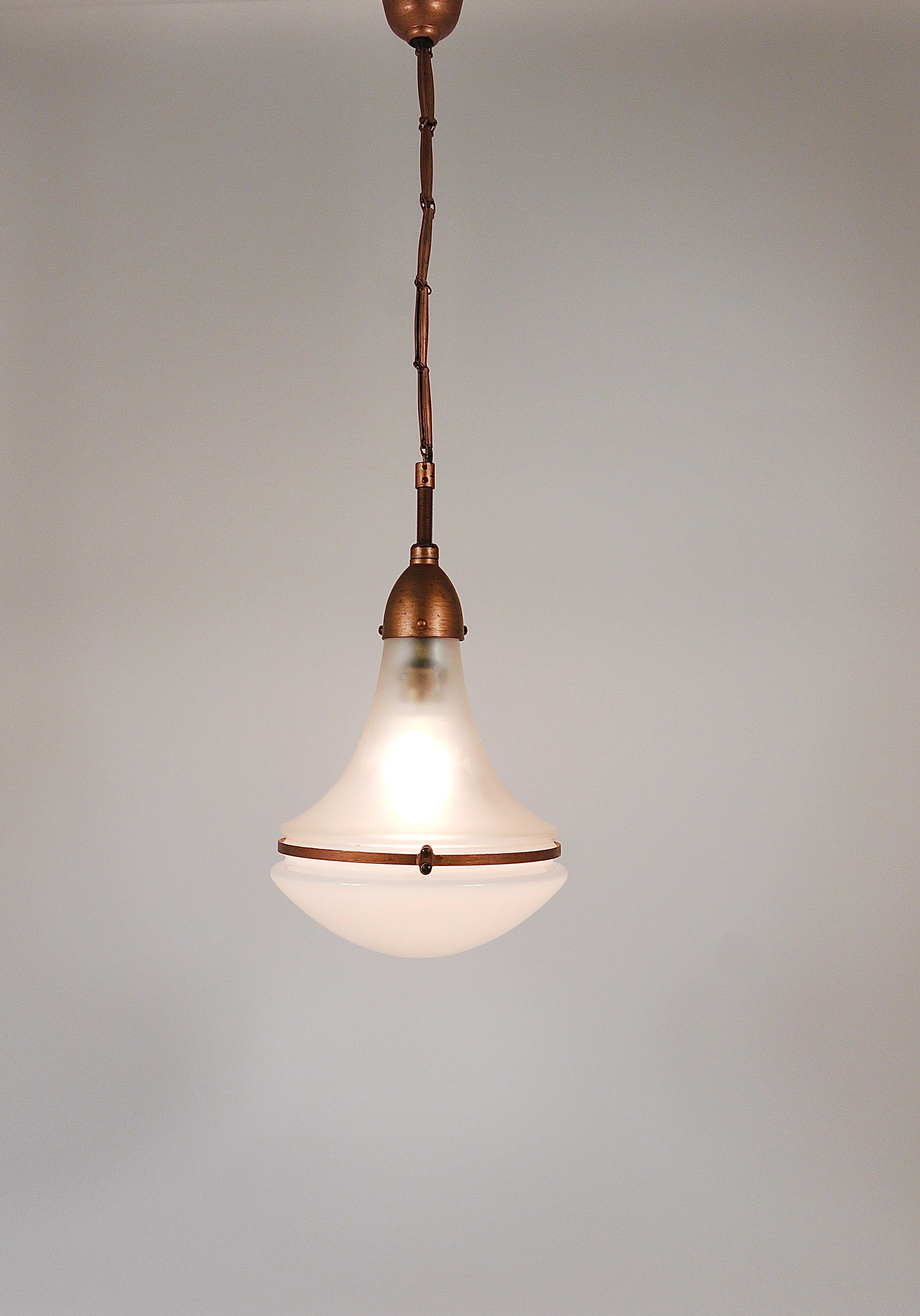 Questa lampada decorativa a sospensione, risalente agli anni '10-'20, è stata progettata da Peter Behrens per Siemens & Schuckert in Germania. Il caratteristico paralume presenta una forma a goccia, realizzata con due diversi tipi di vetro. La parte