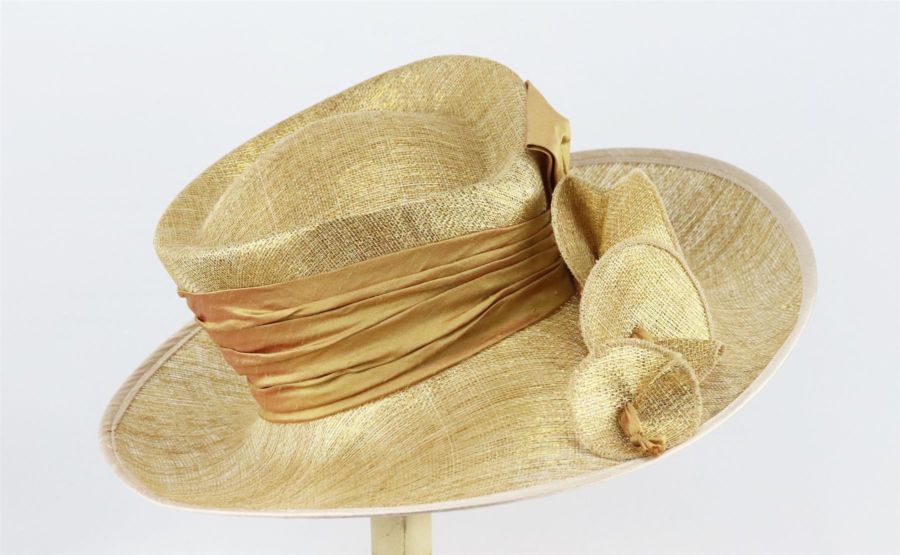This hat by Peter Bettley from Harrods is made from metallic gold sinamay straw in a structured sweeping silhouette and finished flowing bow detail and sash along the front. Gold straw. Slips on. 100% straw. Comes with box. Dimensions: H 7 x W 16.7