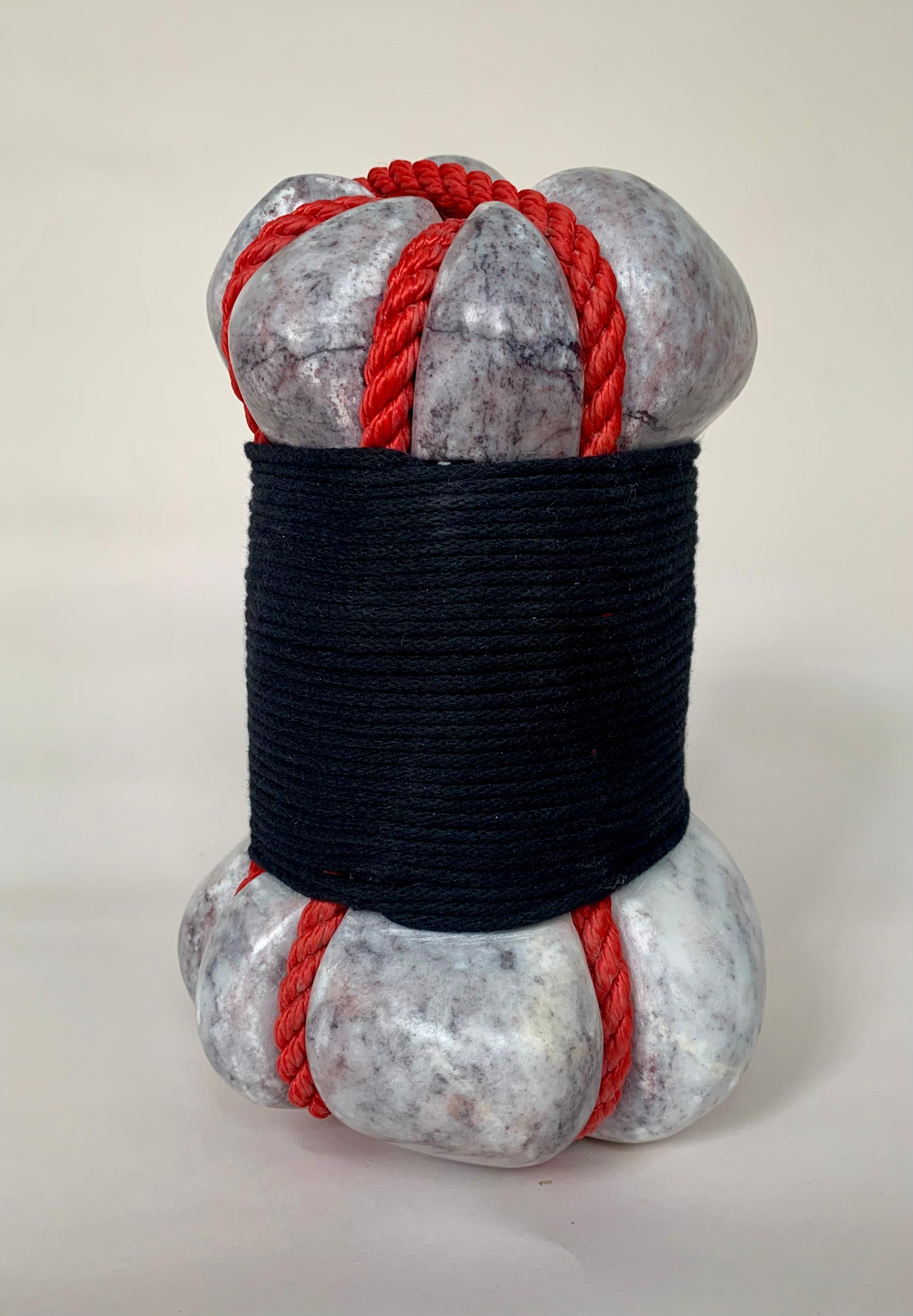 Squeeze is a sculpture by the contemporary British artist Peter Brooke-Ball, made of carved marble wrapped in string and rope. The smooth, rounded stone appears to be tightly compressed by a bright red rope, while a thick band of black string wraps