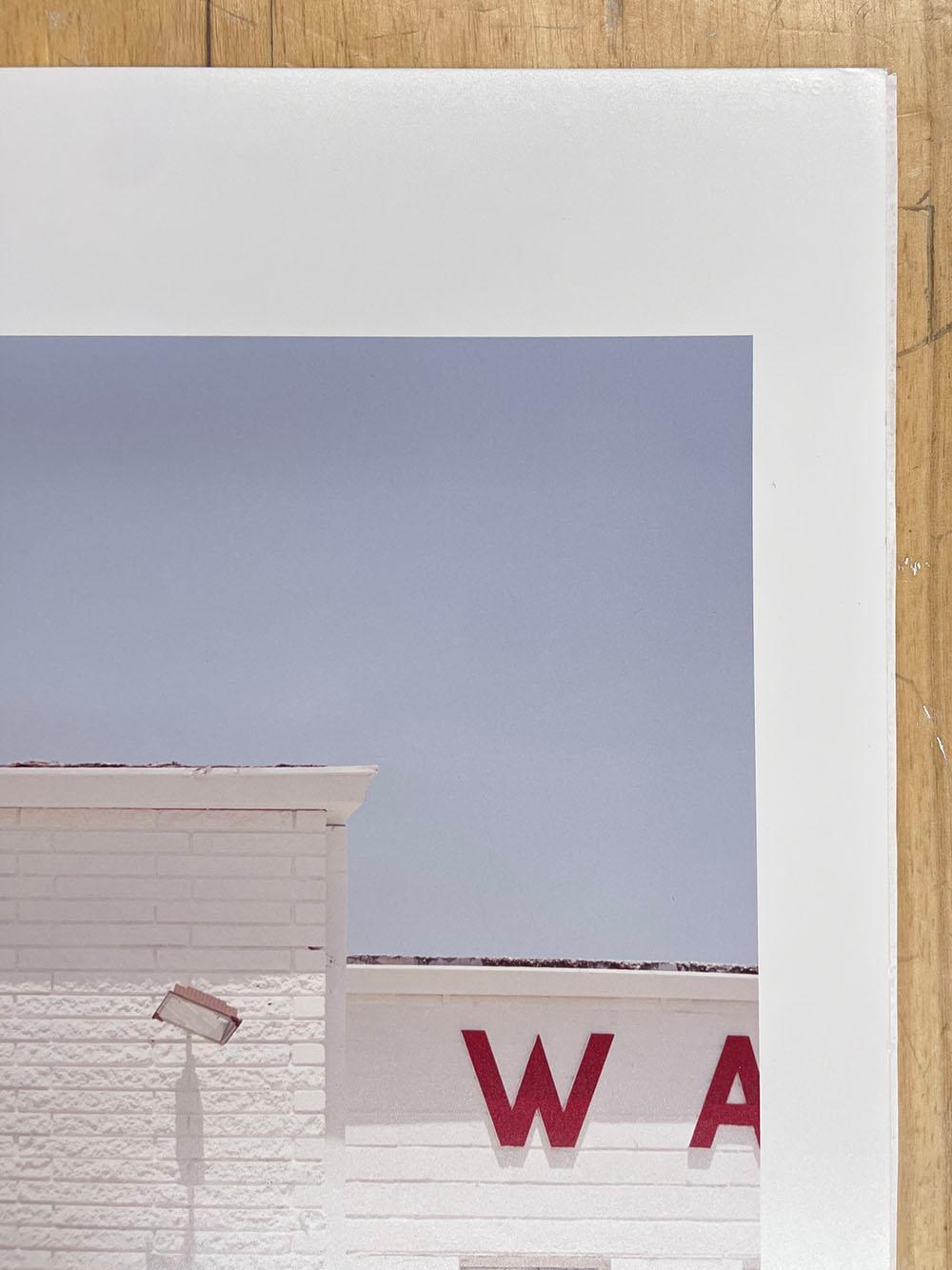 Wash 50 cents by Peter Brown is a color photograph depicting a white laundromat building, with a minimal sign stating 