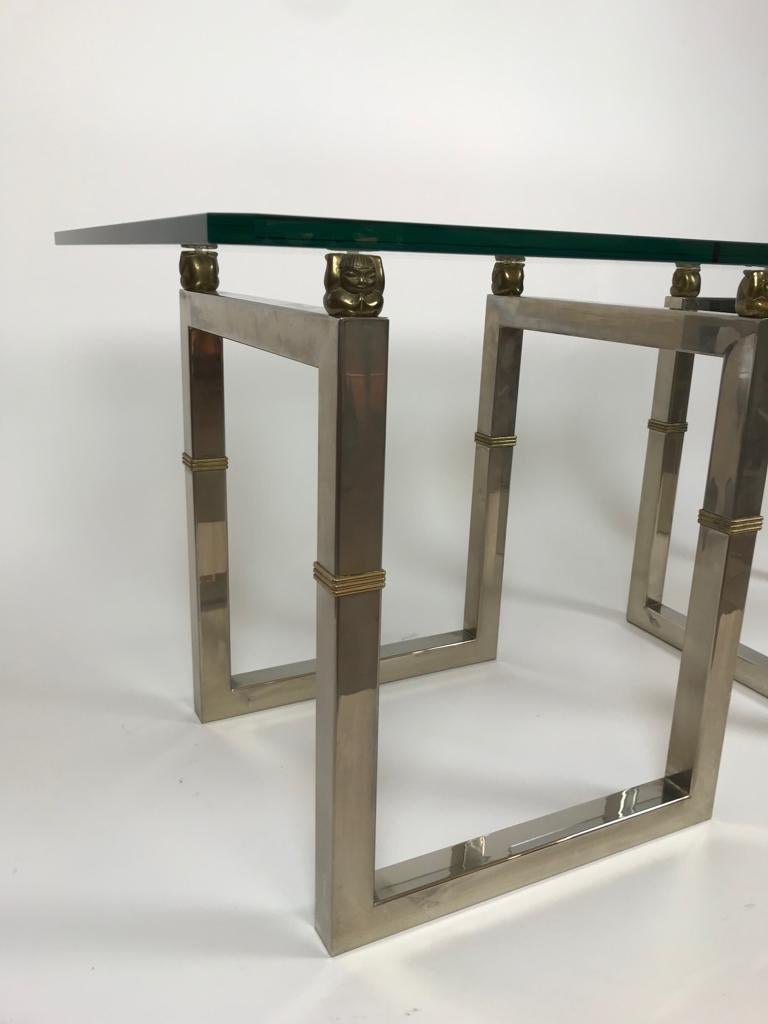 A wonderful pair of Biri T29 side tables by the designer Peter Ghyczy.
They have stainless steel metal legs with a cubic design and a glass top supported by brass Buddhas in each corner.