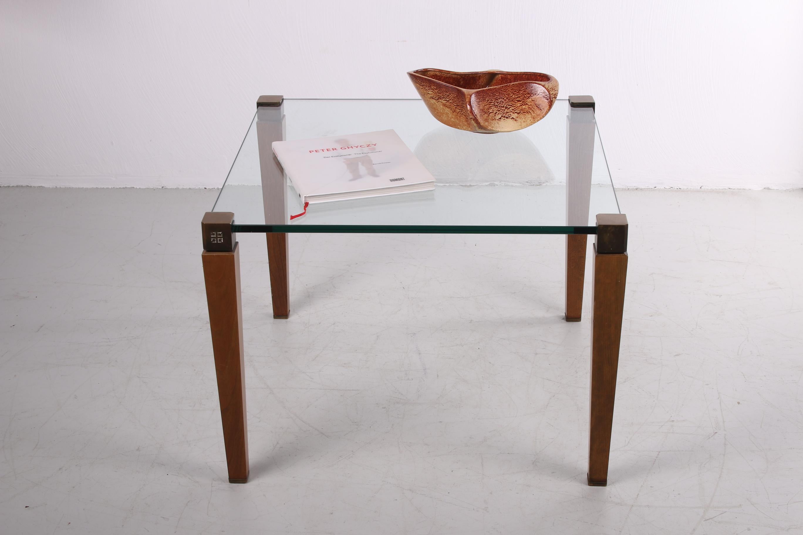 Une belle table basse du designer hongrois Peter Ghyzcy. Cette version a été produite dans les années 1970 aux Pays-Bas.

Cette table basse T56/2 a un plateau en verre transparent et repose sur des pieds en bois avec une tête en bronze