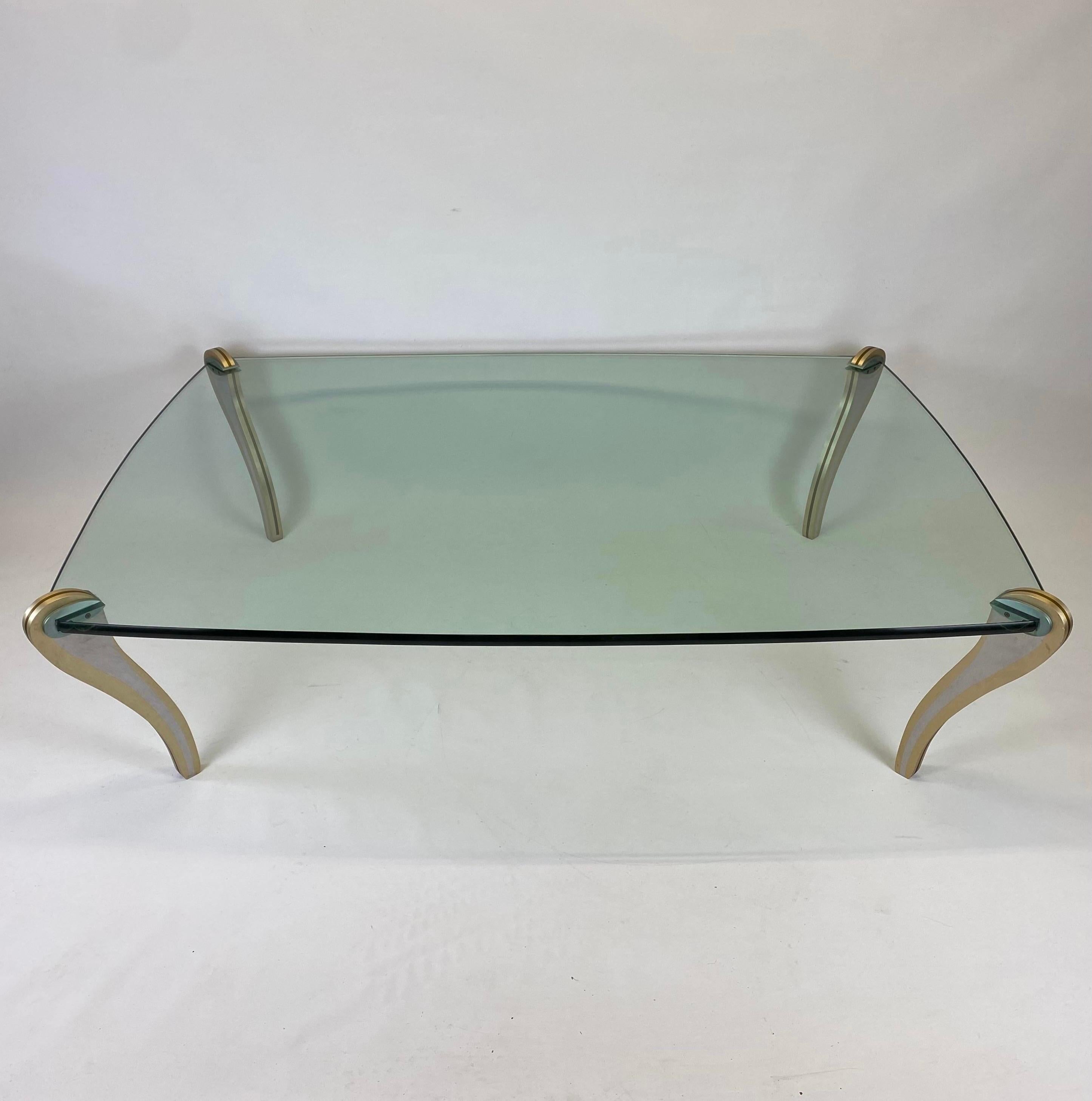An amazing handmade artisan coffee table by Peter Handler for Handler Studio featuring mixed metals sculptural legs attached to a thick shaped glass top. Inlaid metal 