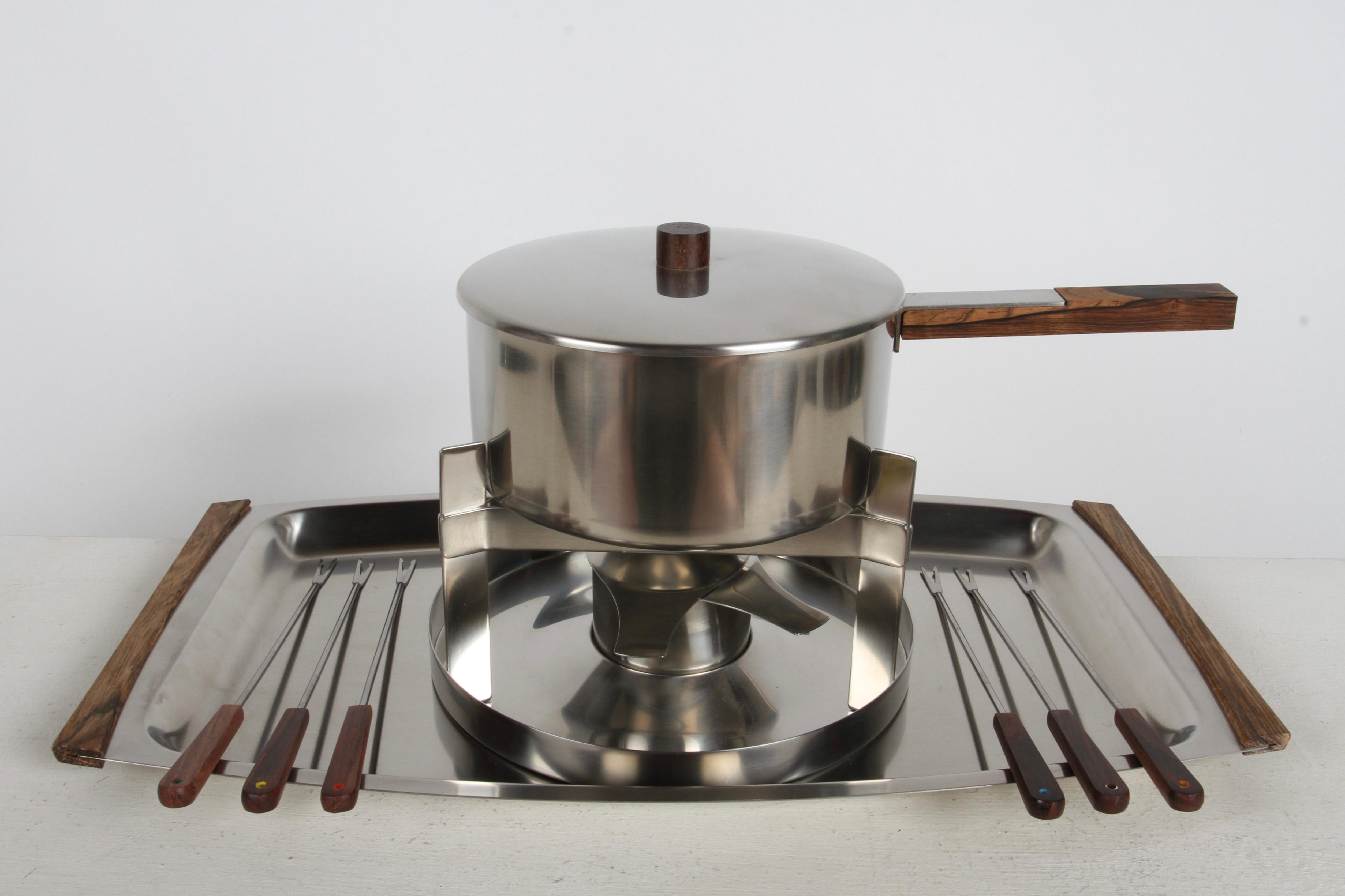 New Old Stock and no longer in production, this 1970s Rosewood & Stainless fondue set designed by or under the leadership of Danish Mid-Century Designer Peter Homblad (stepson from Arne Jacobsen) for Stelton. Made in Denmark, this set comes 11