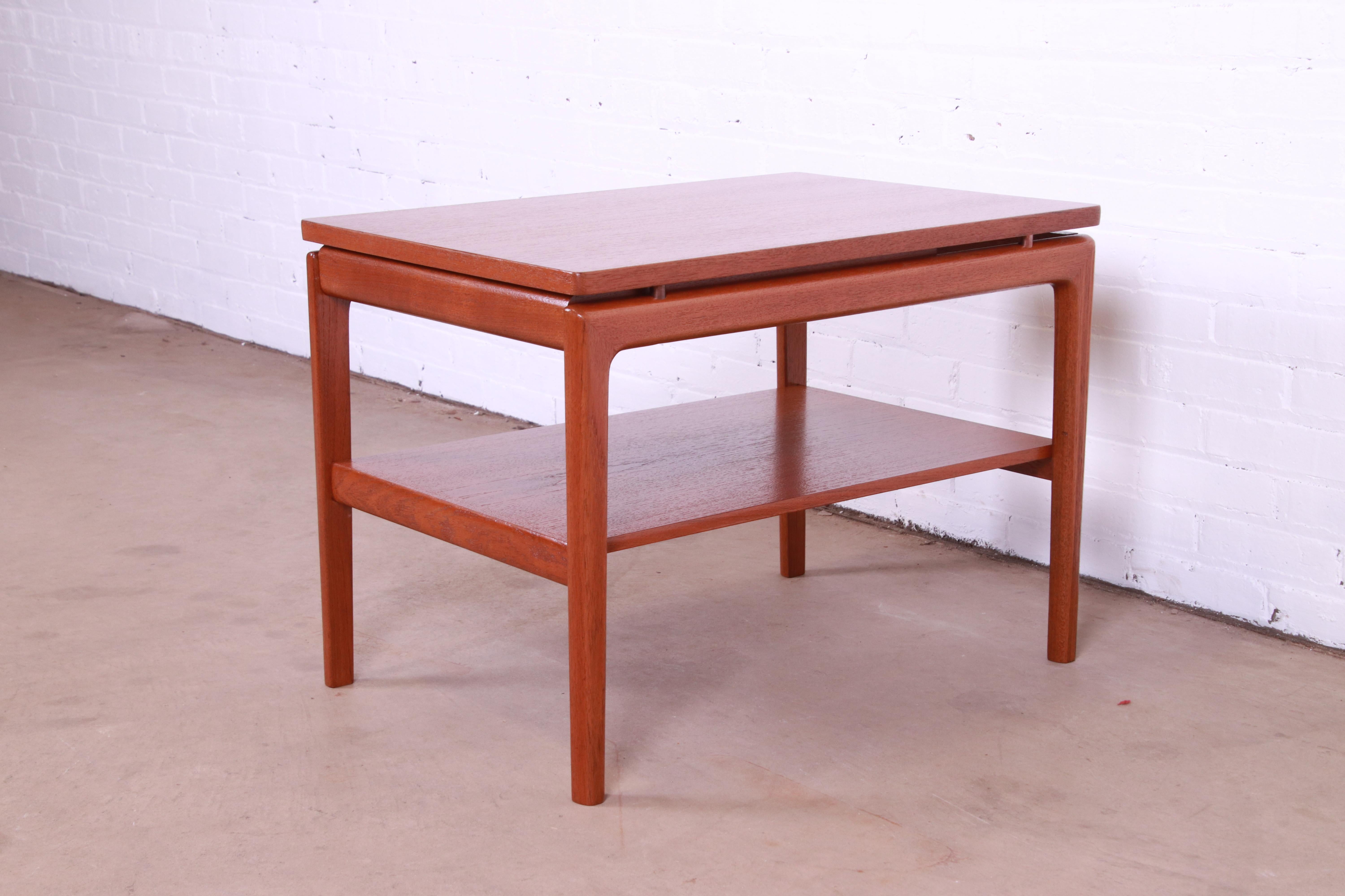 A sleek and stylish mid-century Danish Modern two-tier occasional side table with single drawer

Attributed to Peter Hvidt and Orla Mølgaard-Nielsen

Denmark, 1950s

Sculpted teak, with brass accents.

Measures: 20.5
