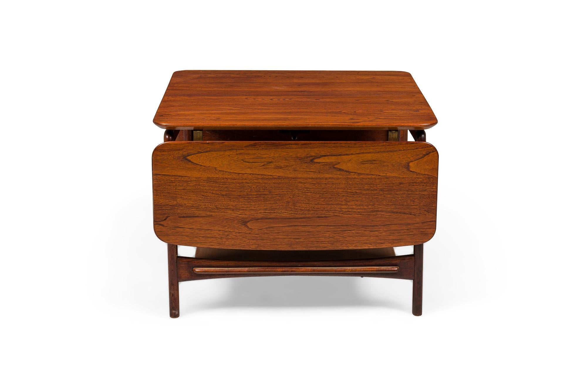 Table d'appoint/de chevet danoise du milieu du siècle en teck carré avec deux feuilles tombantes, supportée par un cadre à quatre pieds avec une étagère à traverse inférieure. (PETER HVIDT)(Tableaux similaires : DUF0381, DUF0382)

2 vis manquantes