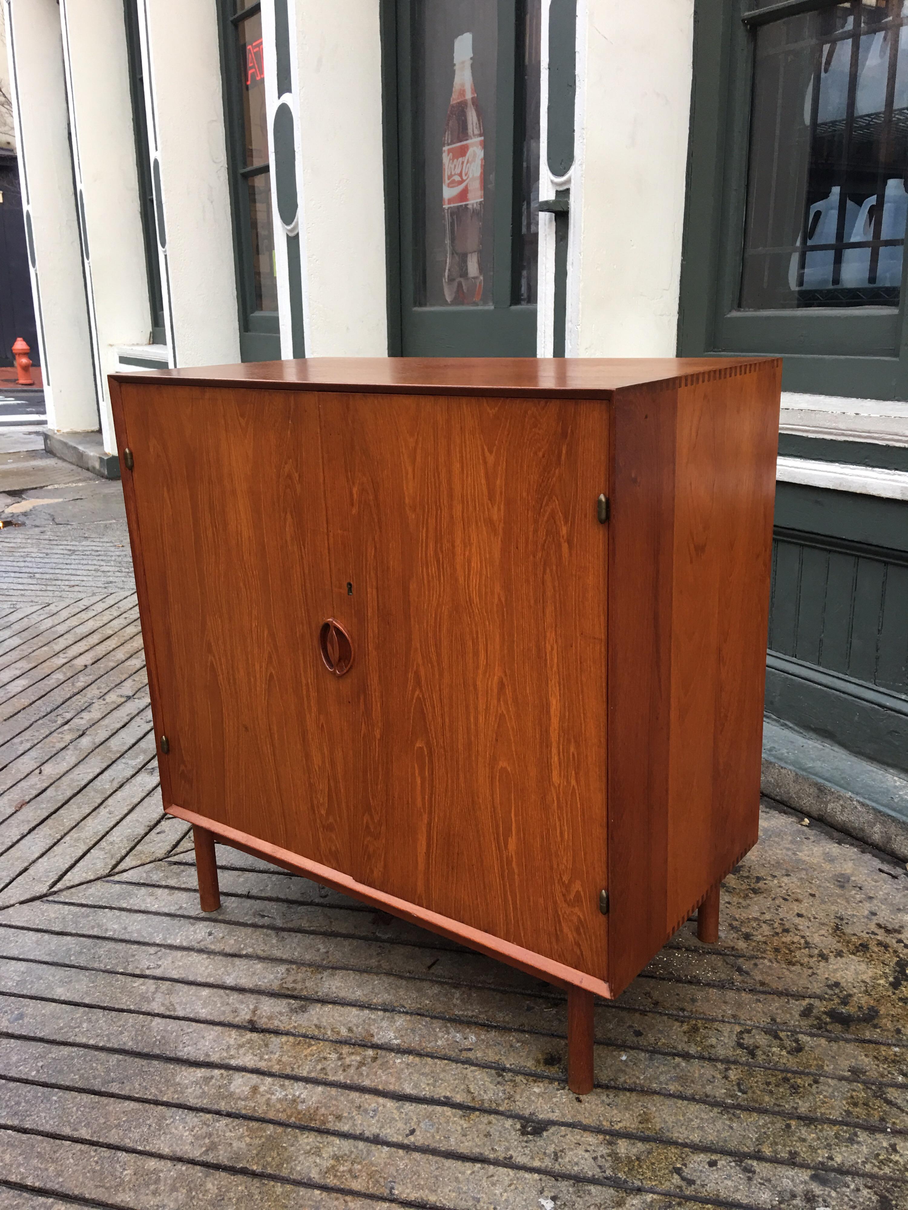 Peter Hvidt for John Stuart teak 2-door cabinet with three slid out drawers and on adjustable shelf. Corners are saw tooth tenon joinery on round cylinder legs.