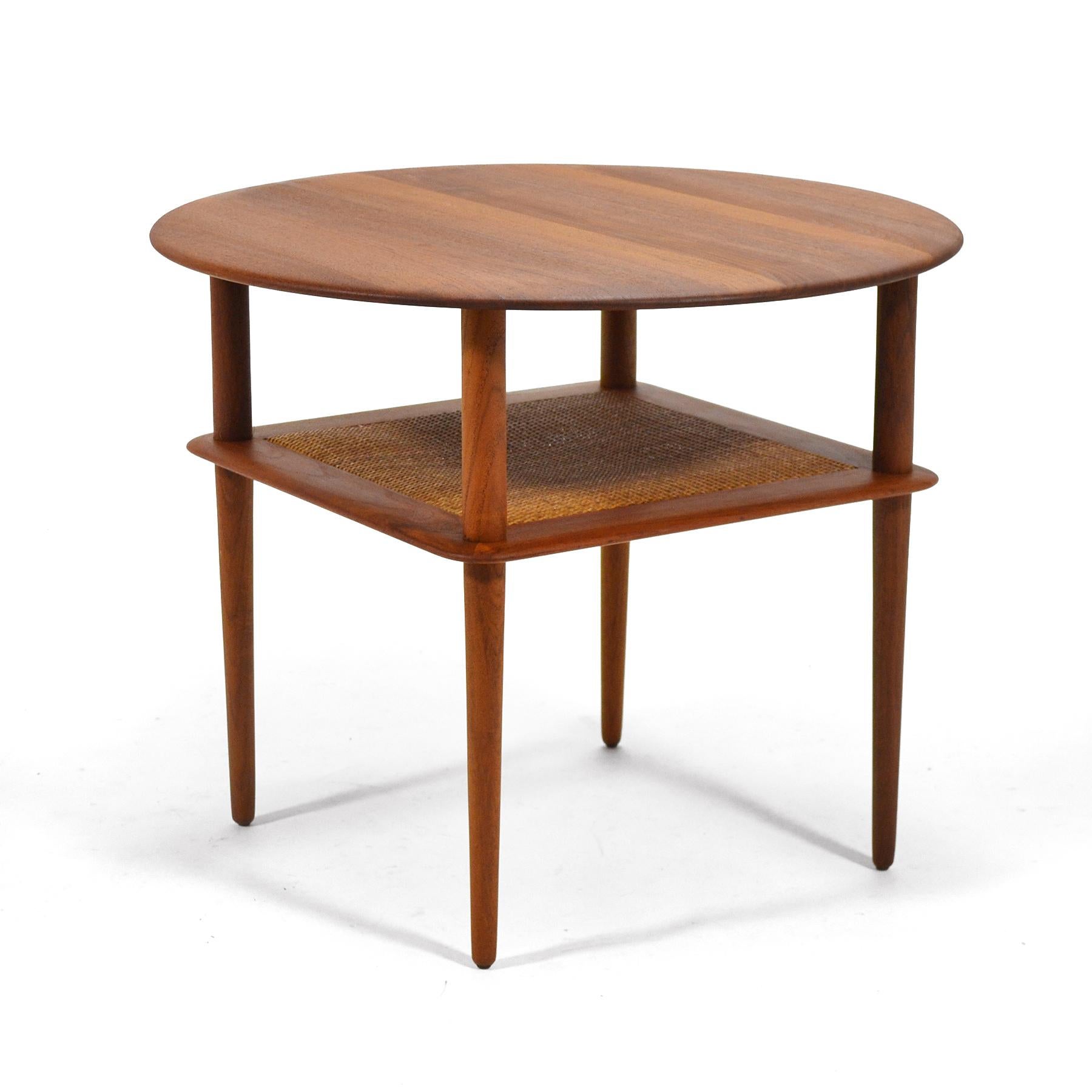 This rare Peter Hvidt & Orla Mølgaard-Nielsen design from 1956 is an uncommon round version of the two-tiered tables designed for France & Daverkosen. It features all solid teak construction and a cane lower shelf. It is marked with a medallion from