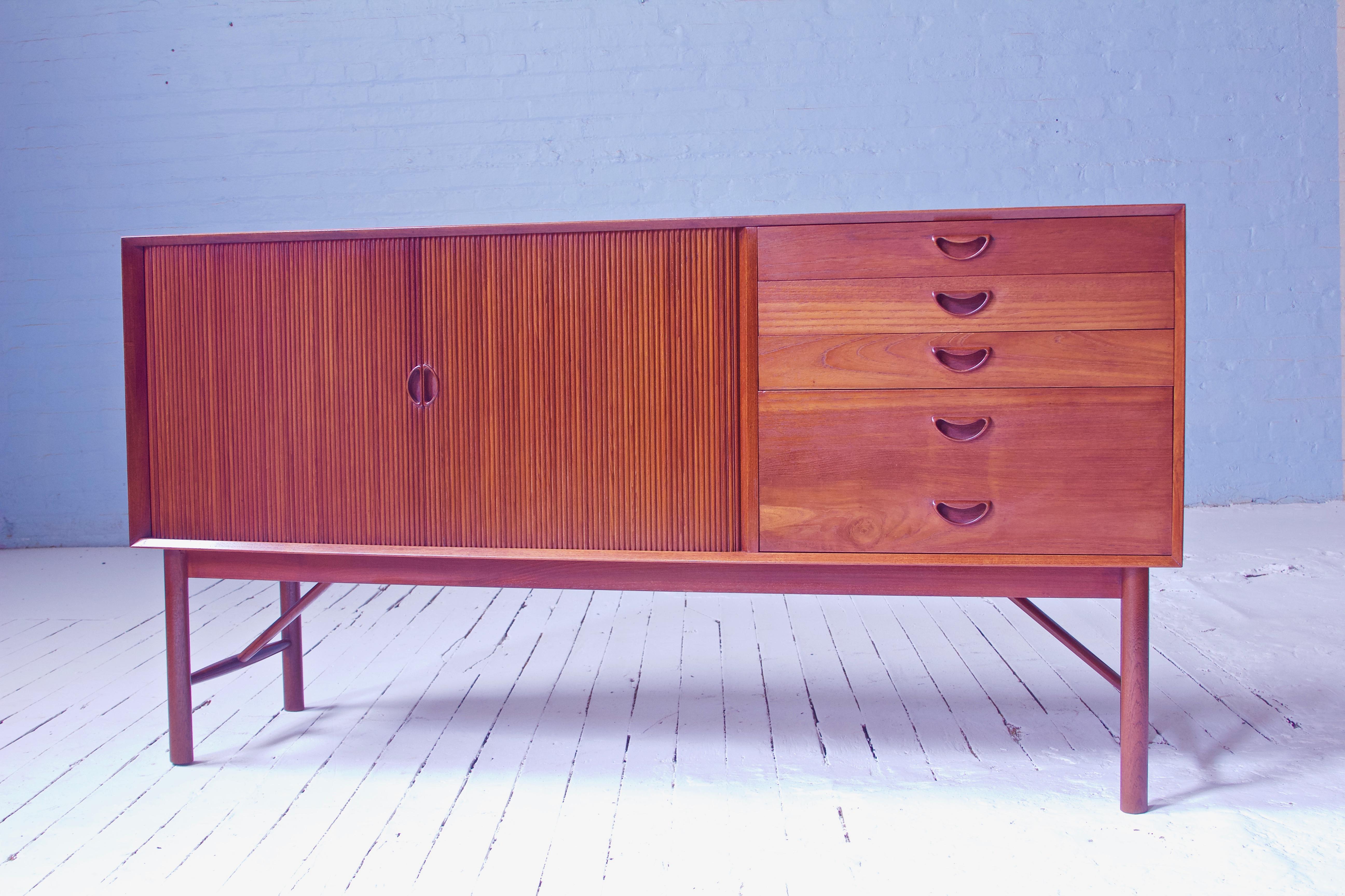 A useful and well-proportioned sideboard by Peter Hvidt & Orla Mølgaard Nielsen featuring exposed finger joinery all around the case, sculpted teak drawer and door pulls, and expertly-executed and perfectly-functioning double tambour doors. Floating