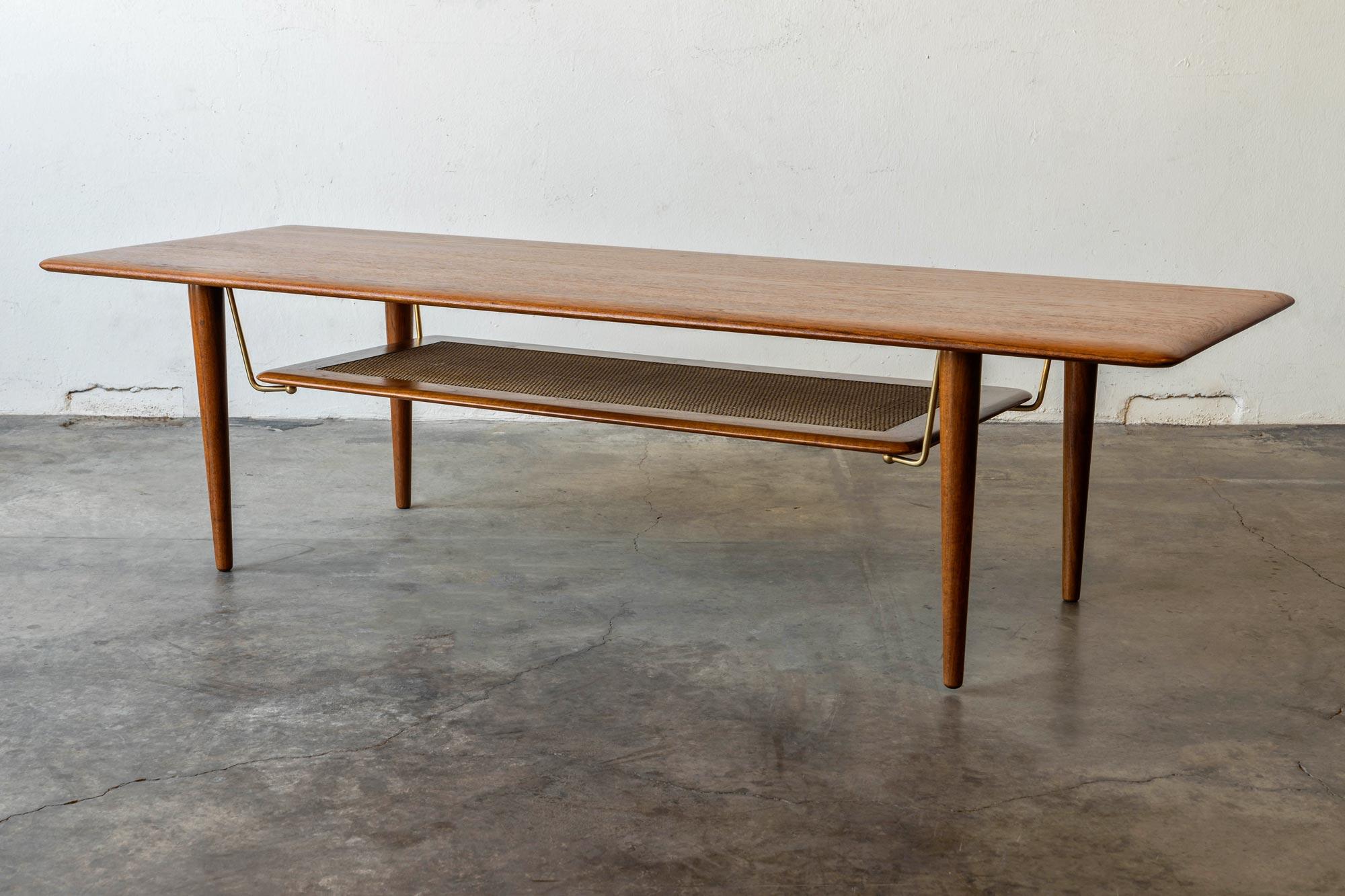 Coffee table set designed in 1956 by Peter Hvidt and Orla Mølgaard Nielsen for France and Daverkosen. The coffee table Model FD516 is composed of a solid teak top / legs with a lower cane rack / shelf suspended by polished brass brackets. The solid