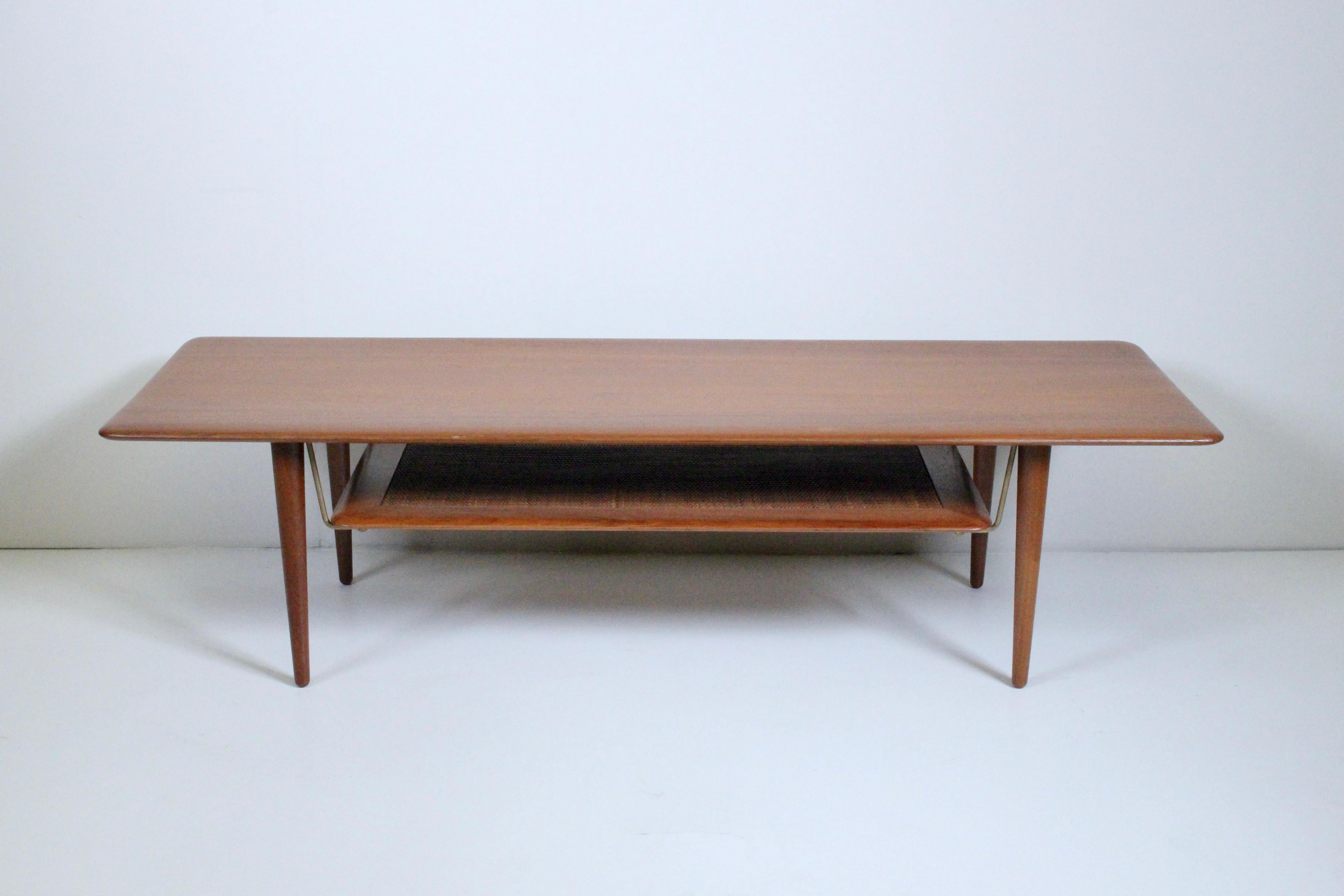 Danish Modern Peter Hvidt & Orla Molgaard Nielsen FD516 Teak Coffee Table. Featuring a rectangular two tier form, four solid turned Teak legs, with smooth, rounded Teak top surface, lower Teak framed Cane shelf detailed with brass fittings. 10