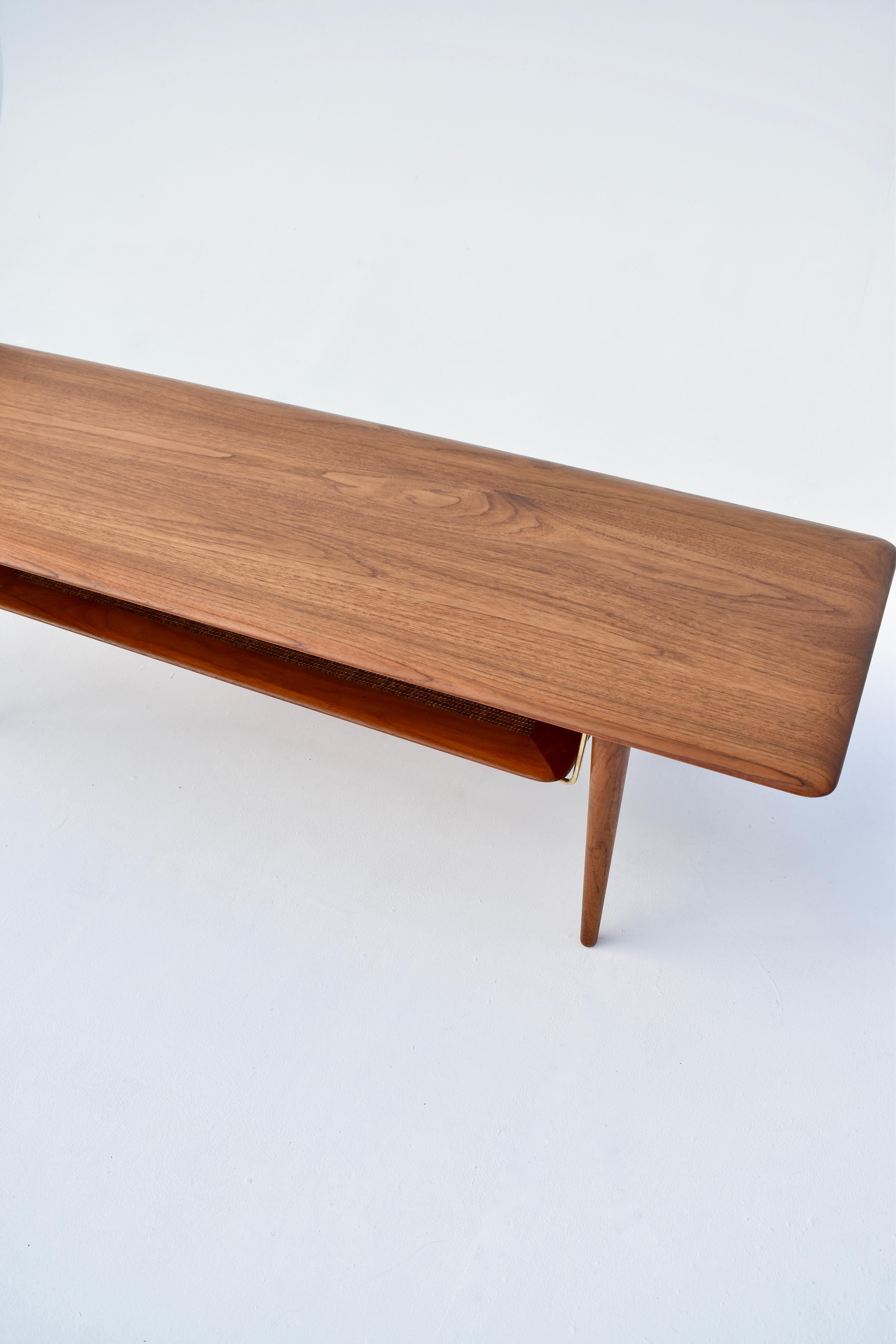 Incredibly elegant long, low coffee table designed in the early 50’s by Architects Peter Hvidt & Orla Molgaard Nielsen.

Constructed entirely from solid Teak with a beautifully profiled surface, beneath is a Rattan shelf suspended on brass
