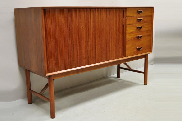 Peter Hvidt and Orla Molgaard Nielsen teak Tambour door Credenza Cabinet for John Stuart. Item features tambour sliding door, unique raised stretcher base, exposed joinery to case, original stamp, working lock and key, 4 dovetailed drawers, 1 wooden