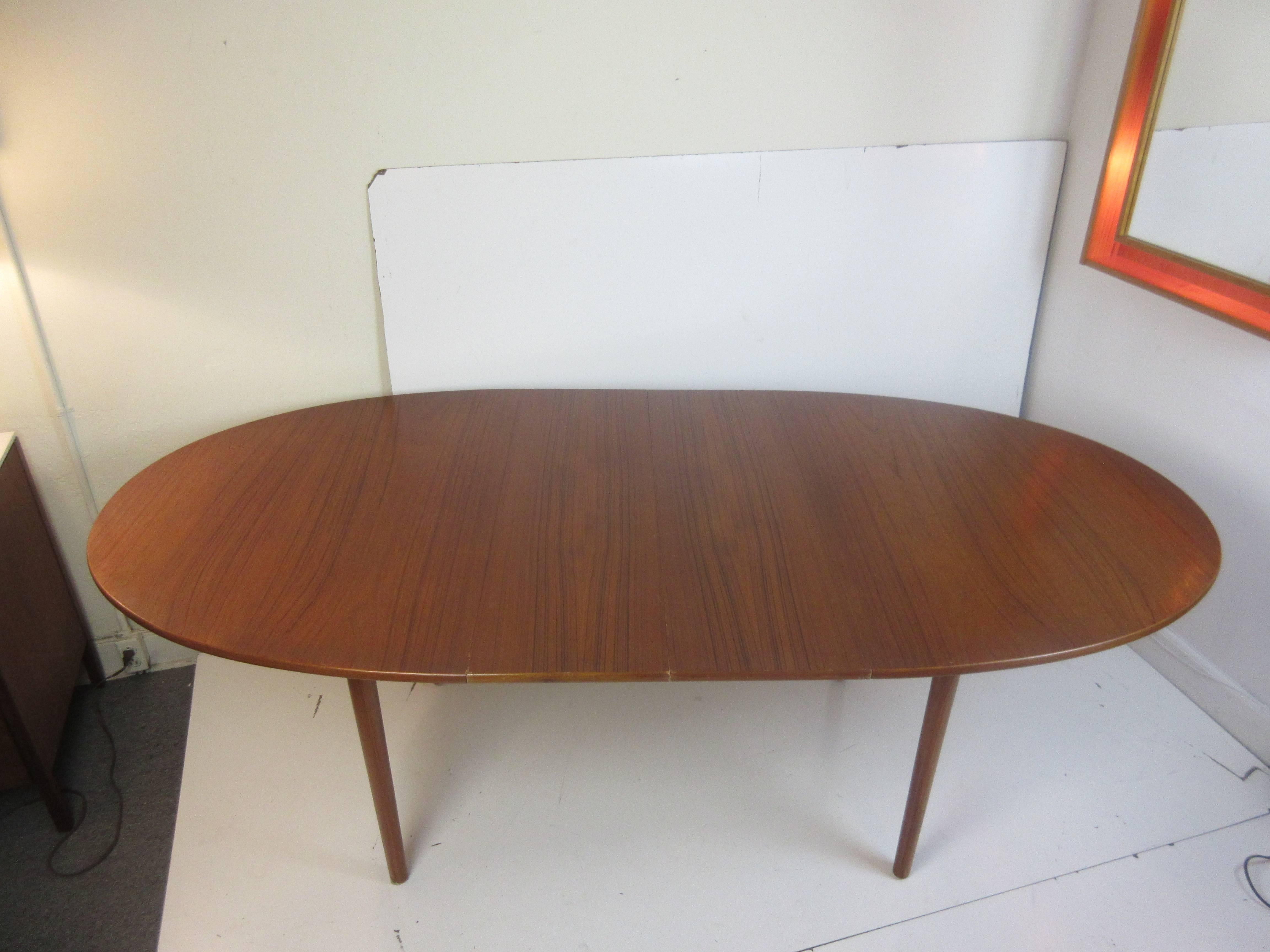 Peter Hvidt teak dining table by John Stuart with two leaves in an oval shape. Table has an inked mark on underside. Each leaf is 12 inches wide. When fully extended table measures 84