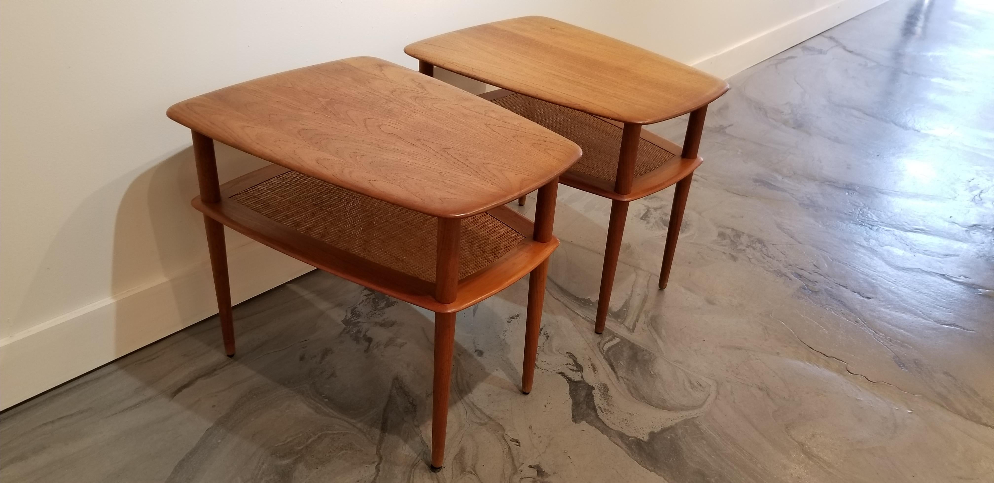 A pair of teak Danish Modern end tables designed by Peter Hvidt for France and Son. Crafted in solid teak with a woven cane magazine shelf under tabletop. Conical legs and woven wicker detail. Tables are in good, original vintage condition with