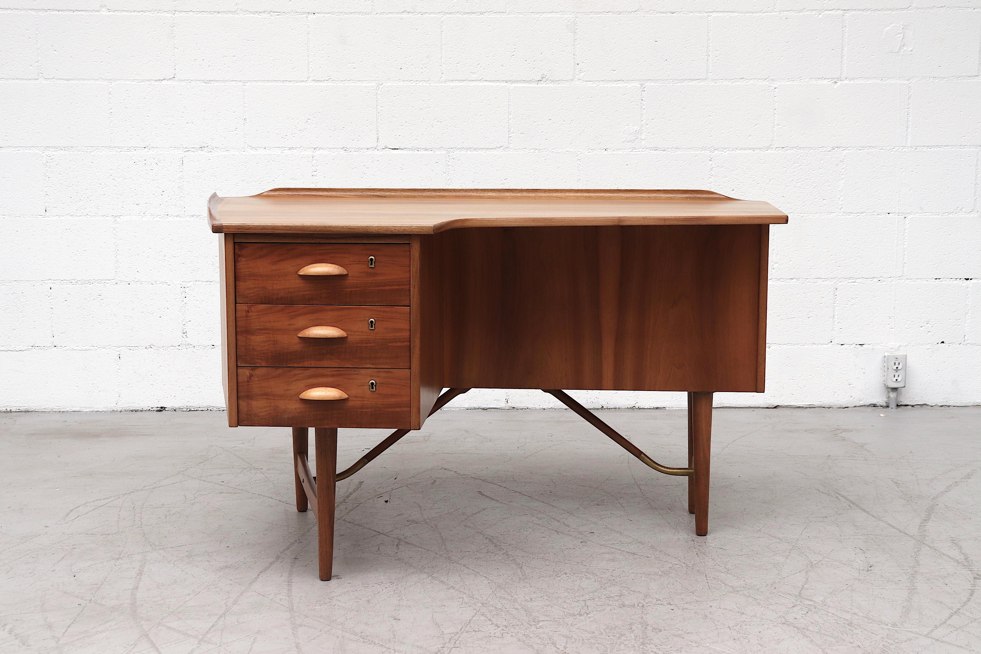 Beautiful Peter Lovig (Attributed) midcentury teak boomerang desk with raised edge, eyelid handles, 3 stacked side drawers with key and built in back bookshelf. Lightly refinished with brass accents, round wood legs. In original condition with