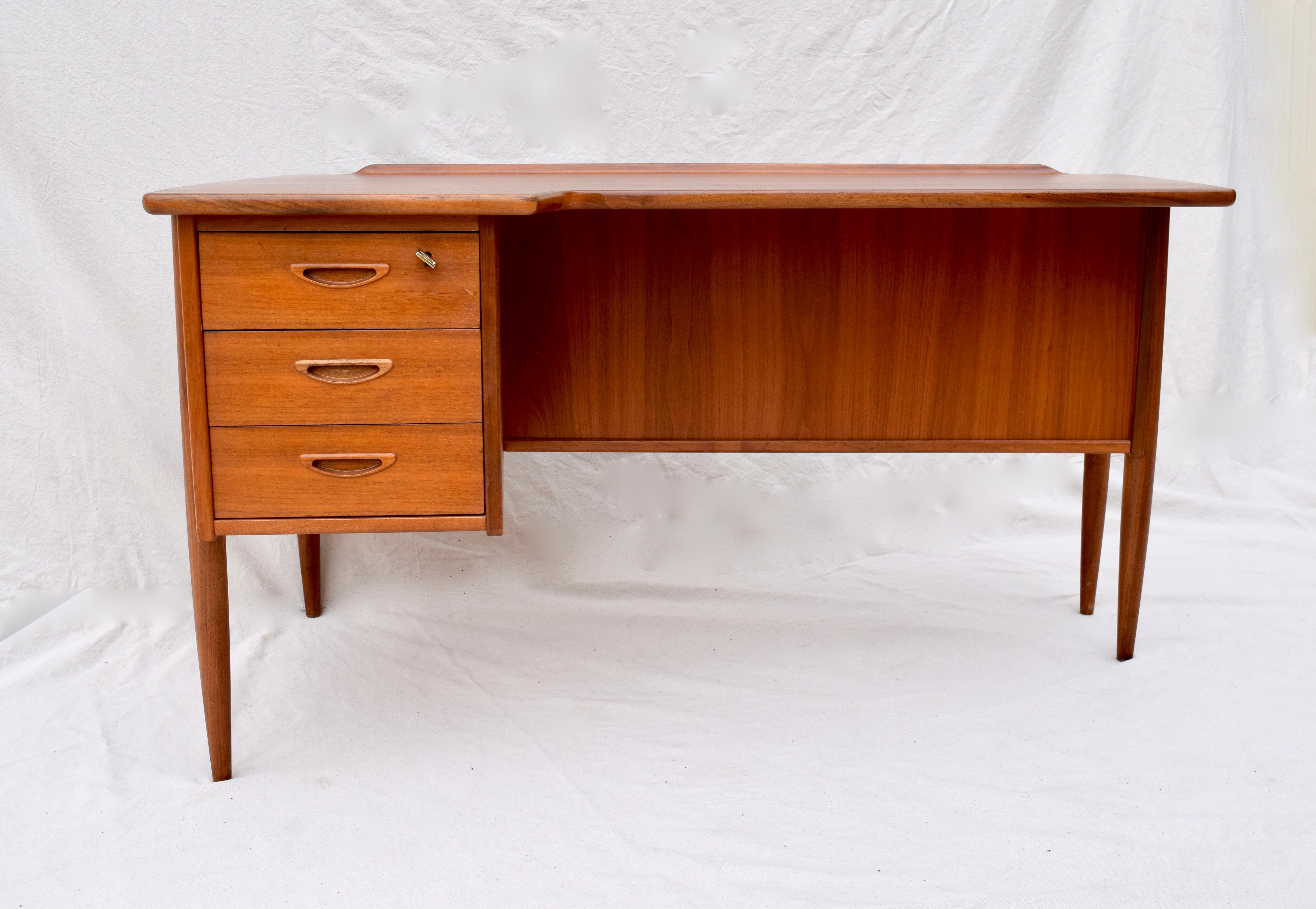 Teak boomerang multifunctional desk designed by Peter Løvig Nielsen, circa 1960. Original finish and keys (2) with working locks, three dovetailed drawers with inlaid handles, drop door cupboard and shelving to the back.