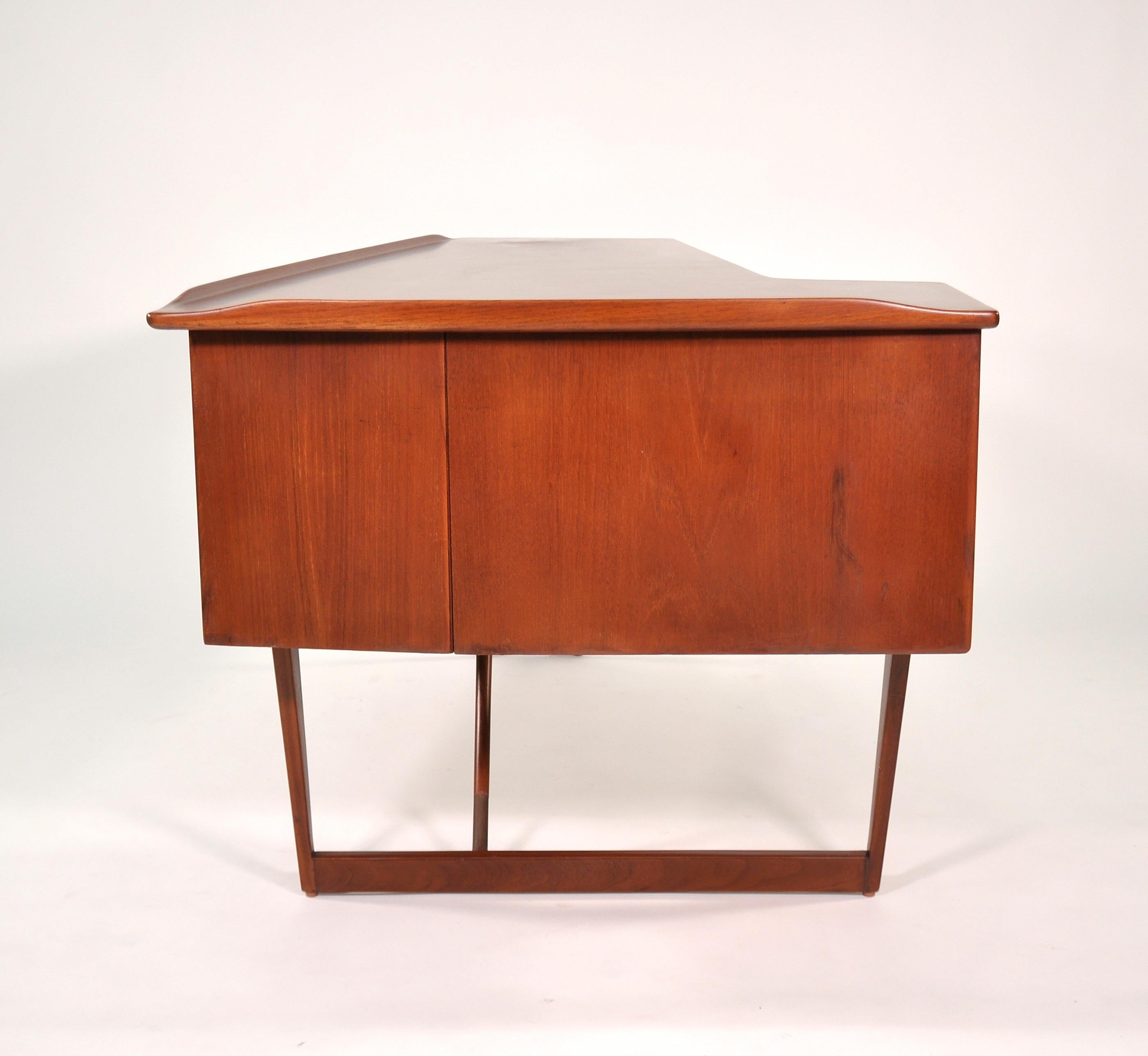 Vintage midcentury Danish modern teak writing table with secret bar by Peter Løvig Nielsen for Dansk Designs, dating from circa 1965. The desk features an L-shaped top over three drawers. The backside features an open bookcase and a cabinet door