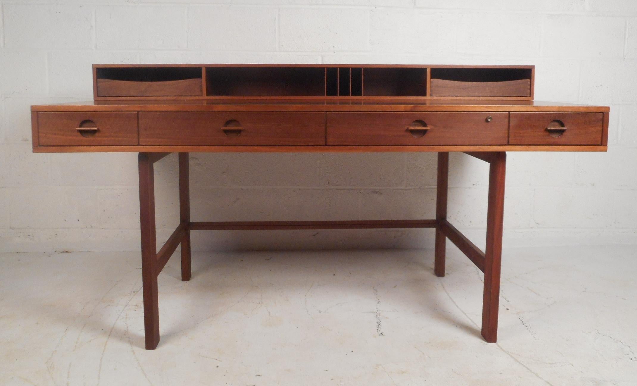 A wonderful midcentury case piece designed by Peter Løvig Nielsen in walnut. This handsome desk features recessed carved drawer pulls and stretchers along the base for added sturdiness. A clever design with a shelf that flips down creating a larger
