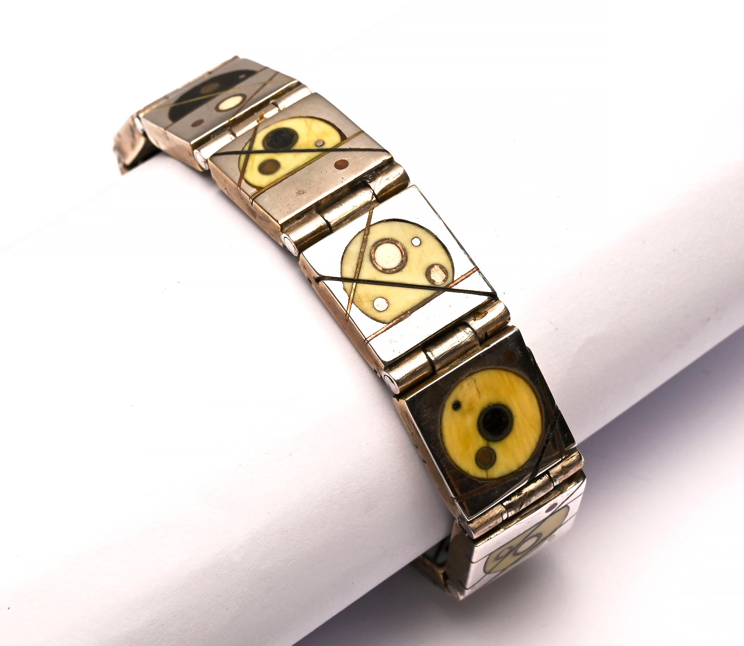 This brilliant, totally reversible bracelet was made by one of the stars of the mid 20th century Modernist jewelry movement, Peter Macchiarini. 
On one side, the nine links are circular designs of onyx; brass; copper and bone on sterling silver.