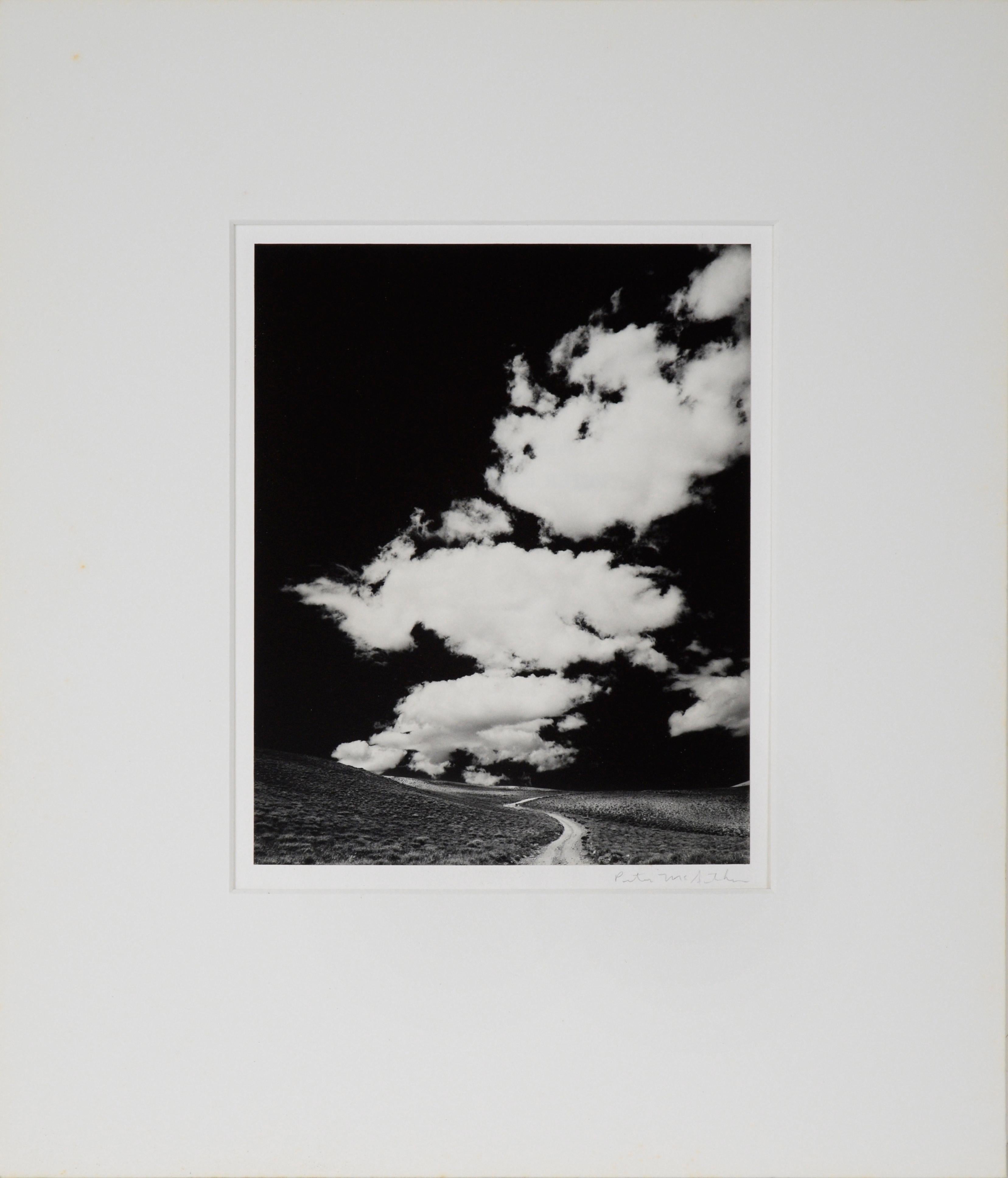 "White Mountains Road With Clouds, 1968" - Black and White Photograph

Black and white photograph depicting a gravel dirt road through the mountains with vibrant white clouds contrasting with the dark sky by Peter McArthur (American, b. 1947).
