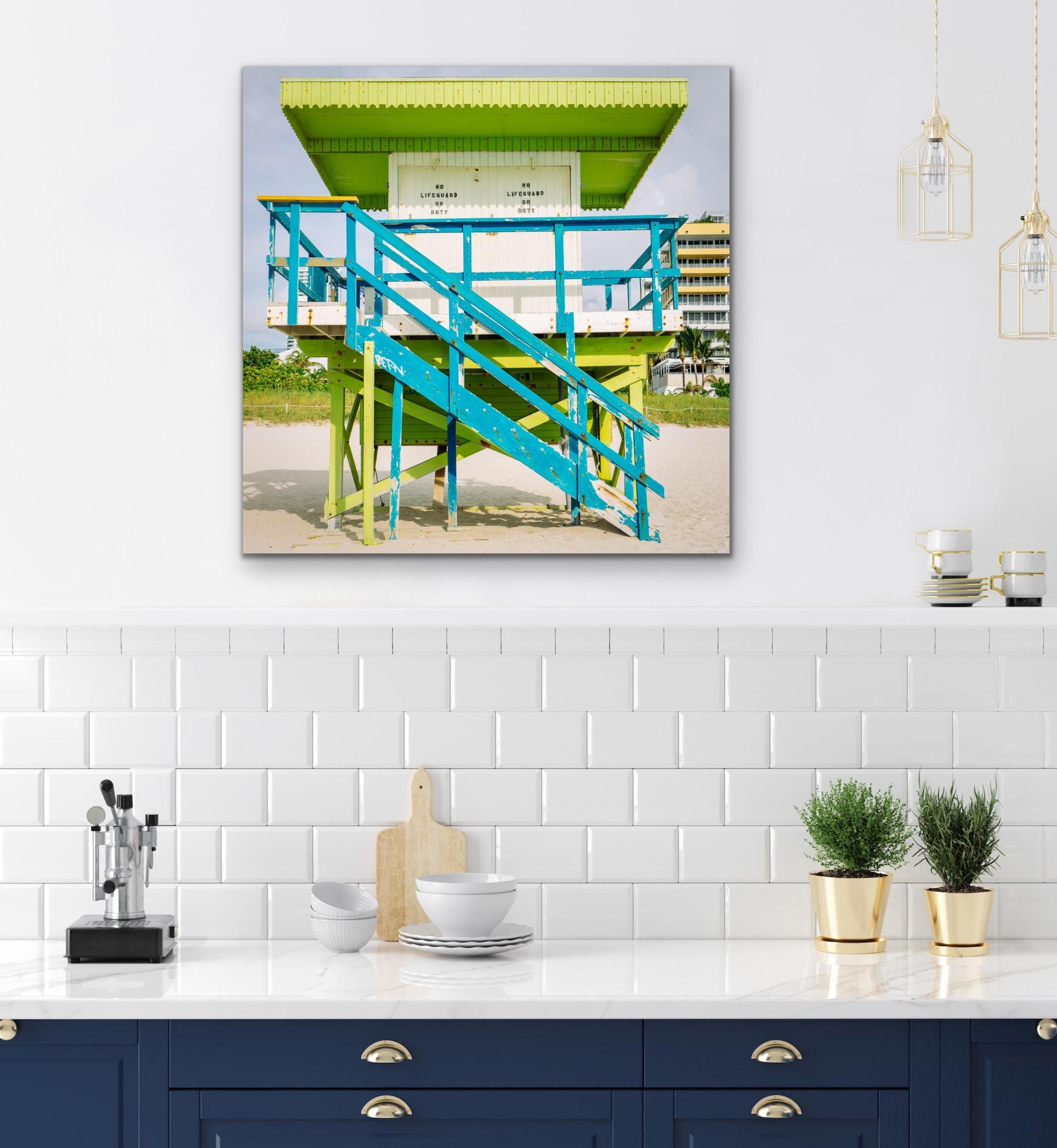 This contemporary coastal photograph by Peter Mendelson depicts a bright blue, lime green and white lifeguard stand  in Miami Beach, Florida. The stand, which has white shut doors that say 