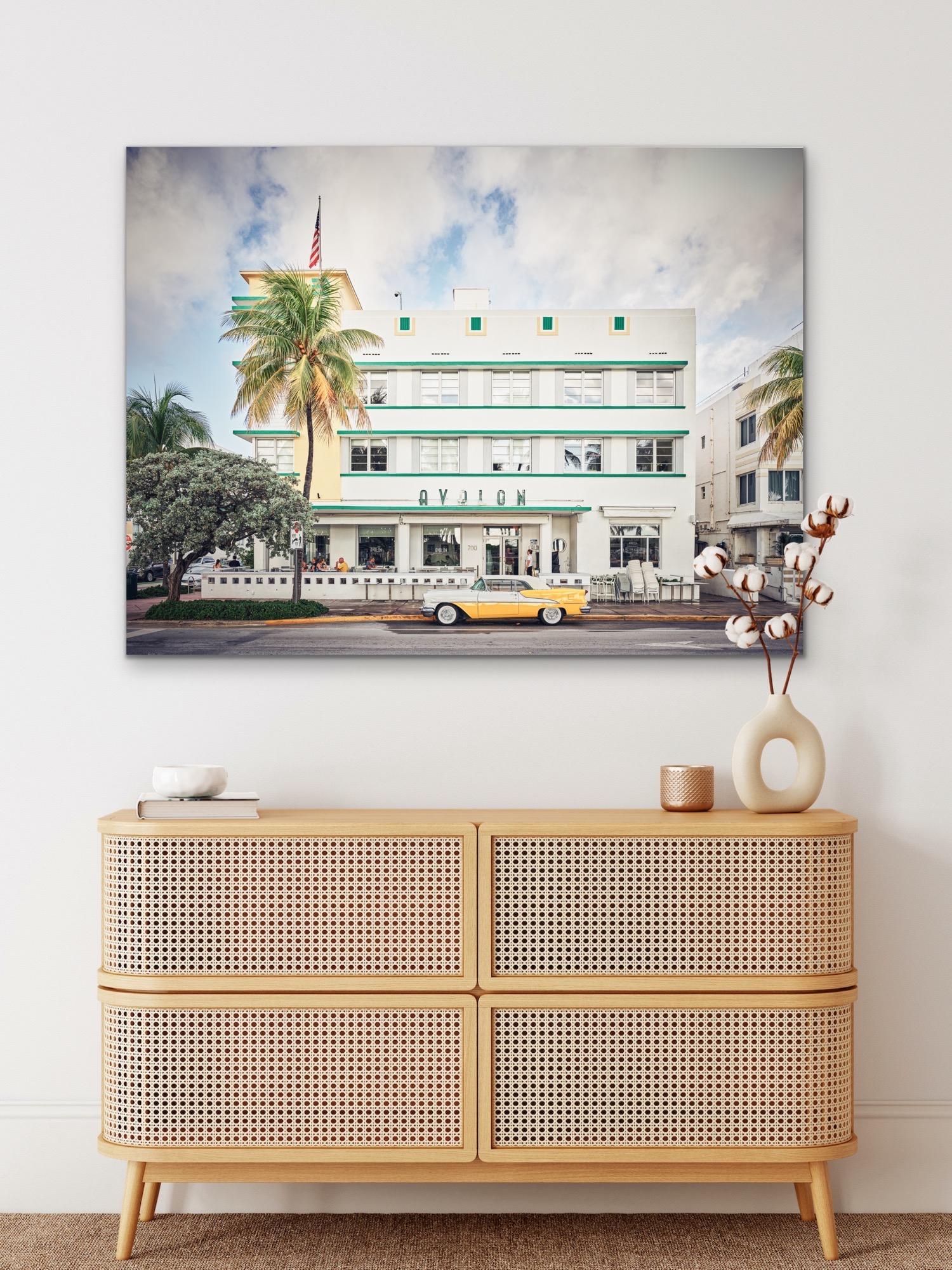 This contemporary urban photograph by Peter Mendelson captures the Deco style Avalon building in Miami Beach, Florida, with a yellow vintage car parked on the street next to a palm tree in front of the building. 

This is a metal sublimation print.
