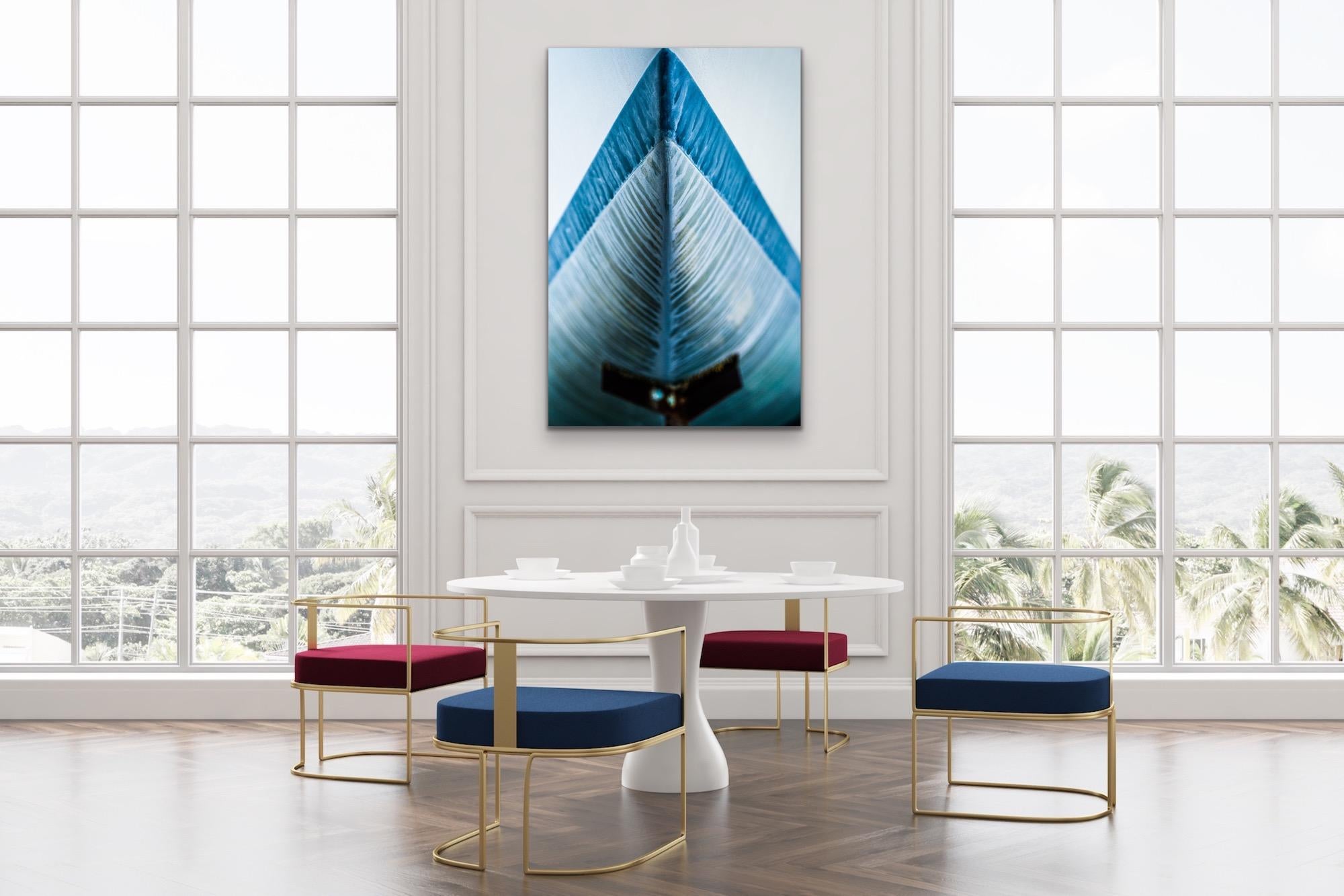 This abstract nautical contemporary photograph by Peter Mendelson pictures a close-up view of a blue boat prow. The image is shot from an angle that creates a triangular shape with a the blue rim of the boat pointing upward. White streaks the blue