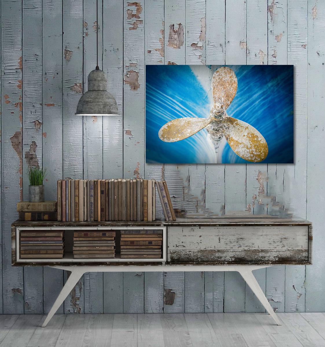 This contemporary coastal photograph by Peter Mendelson features a golden yellow and white boat propeller at the center of the composition, which looks to have had layers of paint chipped and eaten away. The propeller is in perfect focus, with a