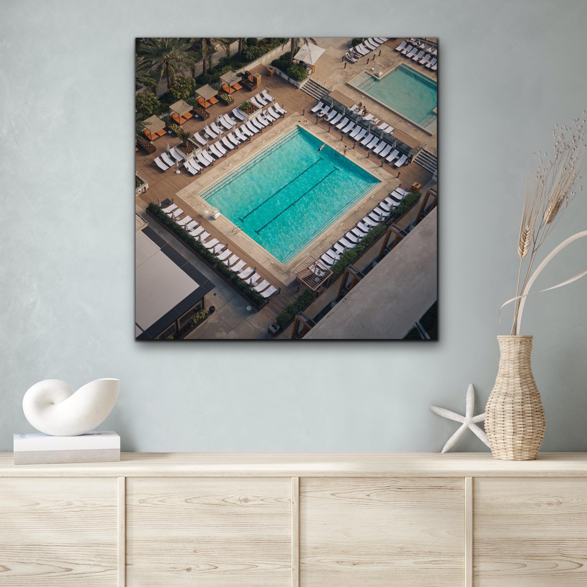 This contemporary photograph by Peter Mendelson captures an angled bird-eye view of a hotel pool in Miami Beach, with a swimmer mid-dive into the still and otherwise empty water. 

This is a metal sublimation print. The frame on an aluminum print is