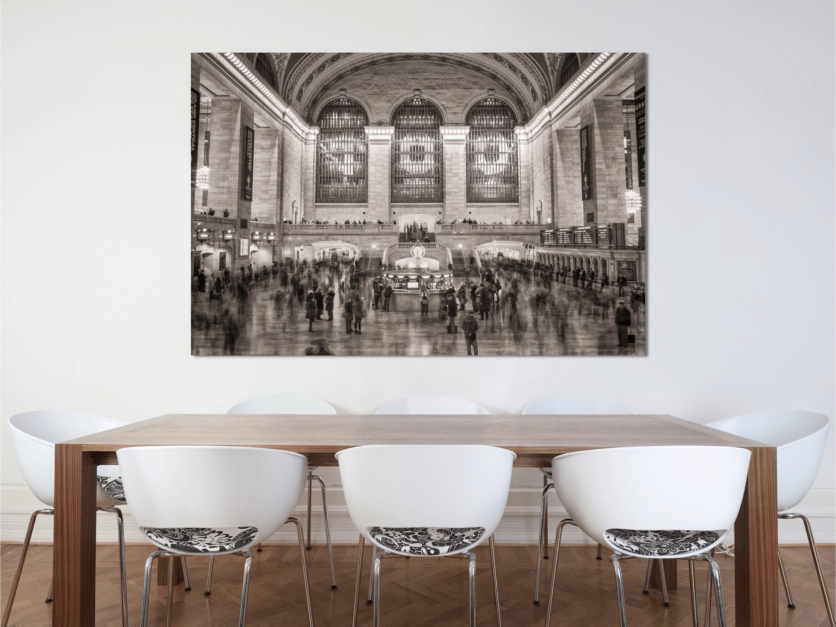 This black and white, urban architectural photograph by Peter Mendelson is taken in Grand Central in Manhattan. Filled with people milling through the large space, some are in focus while others are blurred shadows of movement. The grand