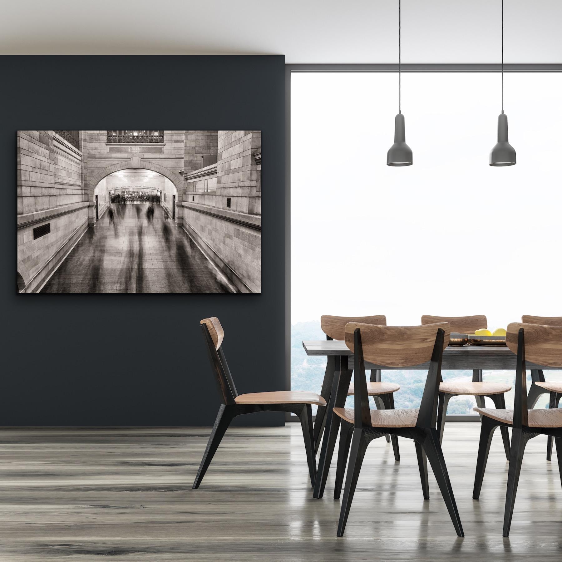 This black and white, urban architectural photograph by Peter Mendelson was taken in Grand Central Station in Manhattan. The artist has captured the still, stately nature of this landmark building, while the moving commuters, tourists, and city