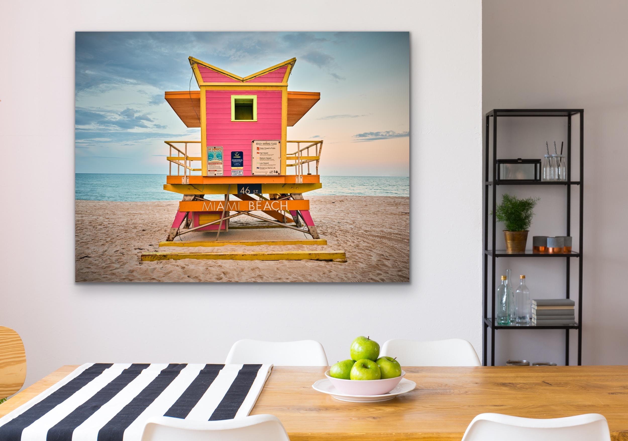 This contemporary coastal photograph by Peter Mendelson features a warm, subtle palette. It captures one of the famously unique lifeguard stands of Miami Beach, Florida, with magenta panelling and yellow and orange trim. The lifeguard stand