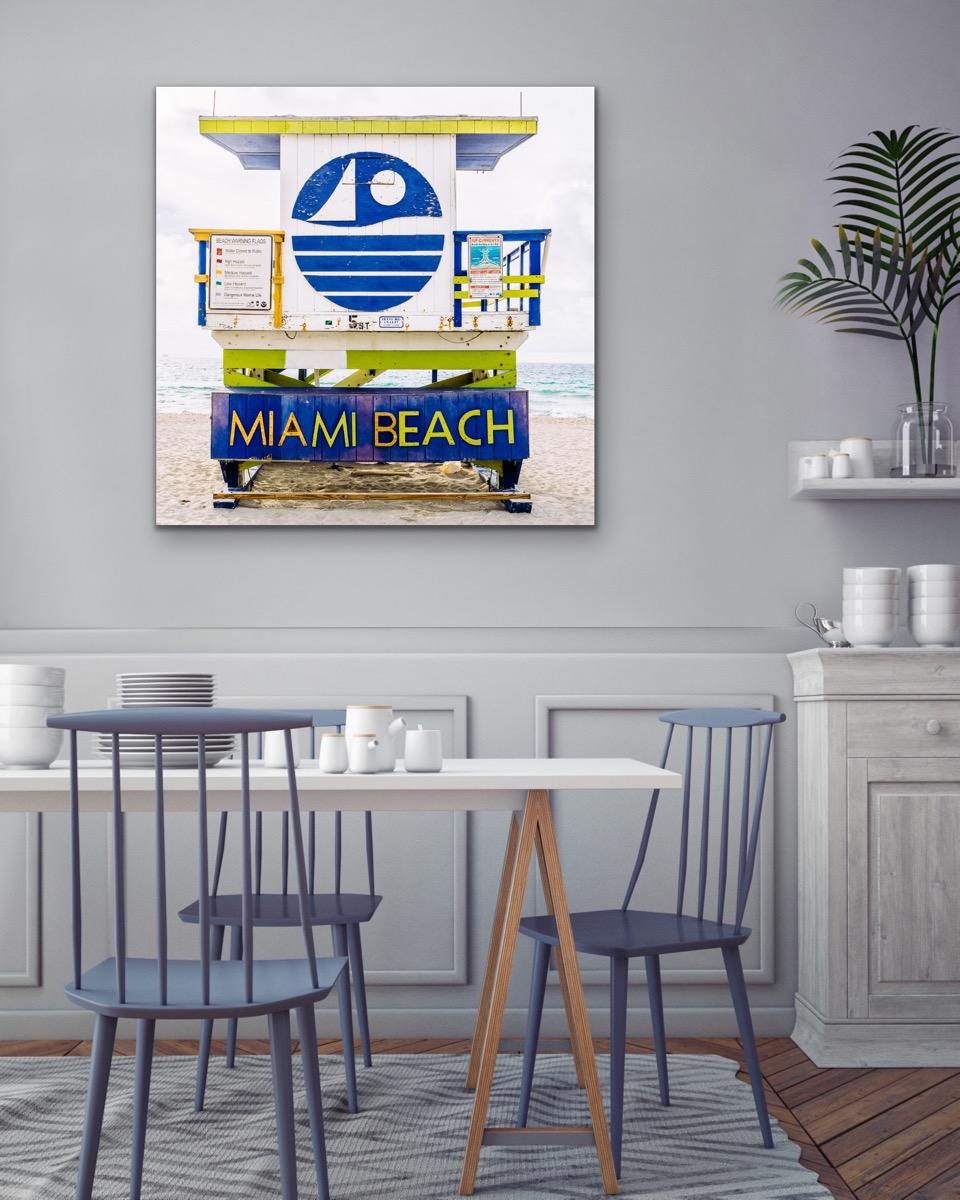 This contemporary coastal photograph by Peter Mendelson depicts a white, deep blue, yellow, and lime green geometric lifeguard stand in Miami Beach, Florida. The structure features a yellow roof, a white-paneled exterior with a geometric painted