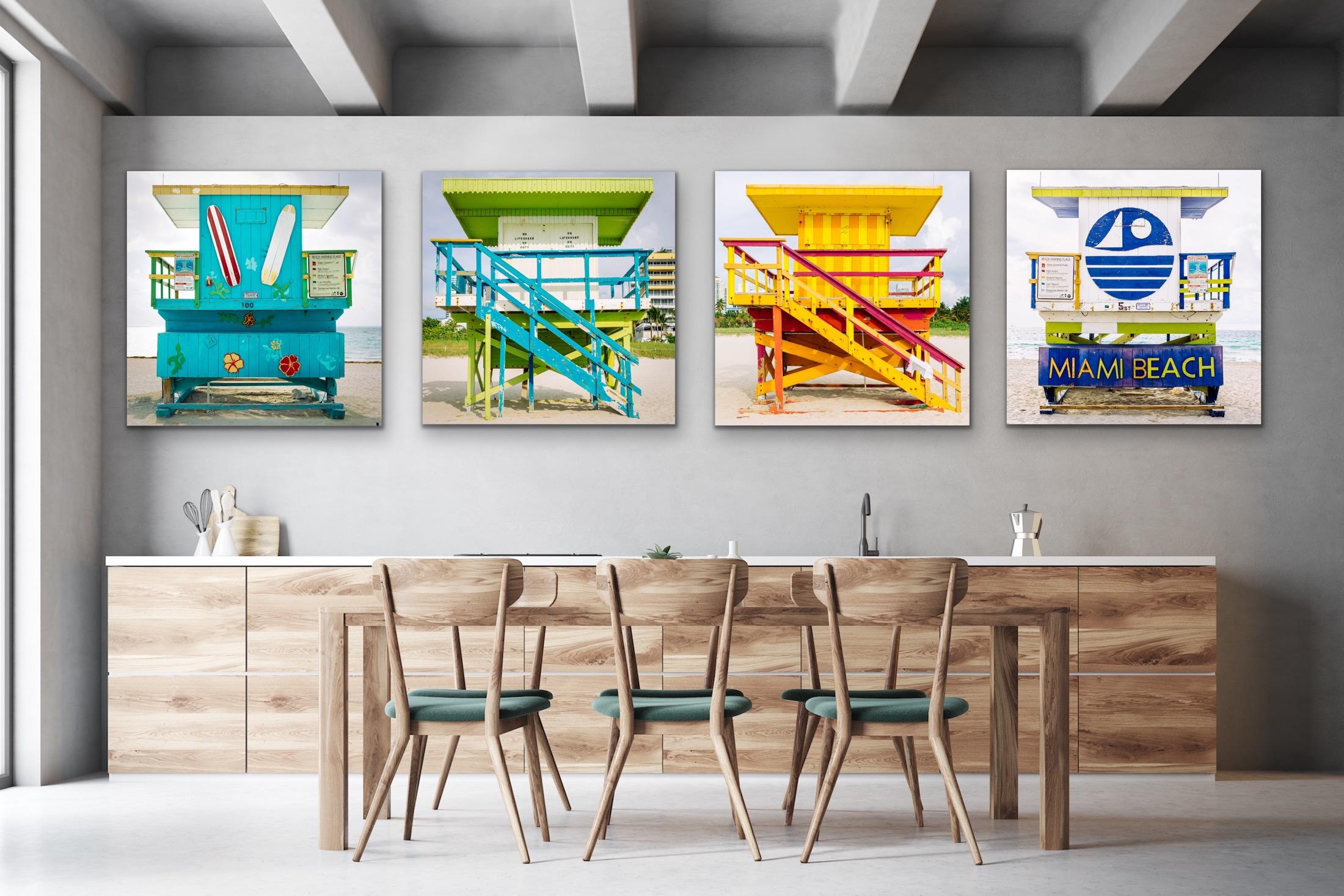 This contemporary coastal photograph by Peter Mendelson features a close-up view of a bright teal, green, and yellow lifeguard stand in Miami, Florida. The blue, vertical panels of the stand are decorated with mounted striped surfboards, painted