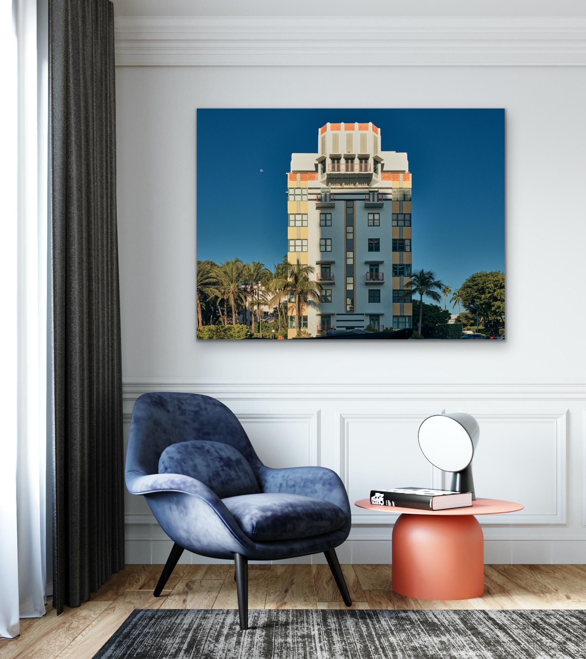 This contemporary coastal photograph by Peter Mendelson features a partially shadowed view of the Deco style Helen Mar building in Miami Beach, Florida, under a clear sky and the moon. It is surrounded by lush palm trees. 

This is a metal