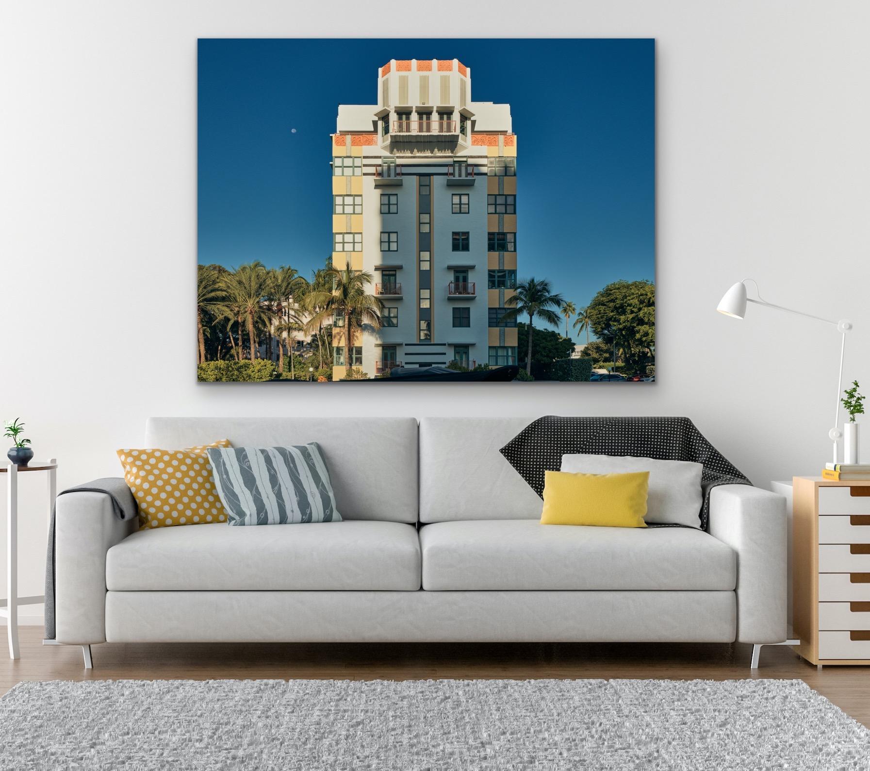 This contemporary coastal photograph by Peter Mendelson features a partially shadowed view of the Deco style Helen Mar building in Miami Beach, Florida, under a clear sky and the moon. It is surrounded by lush palm trees. 

This is a metal