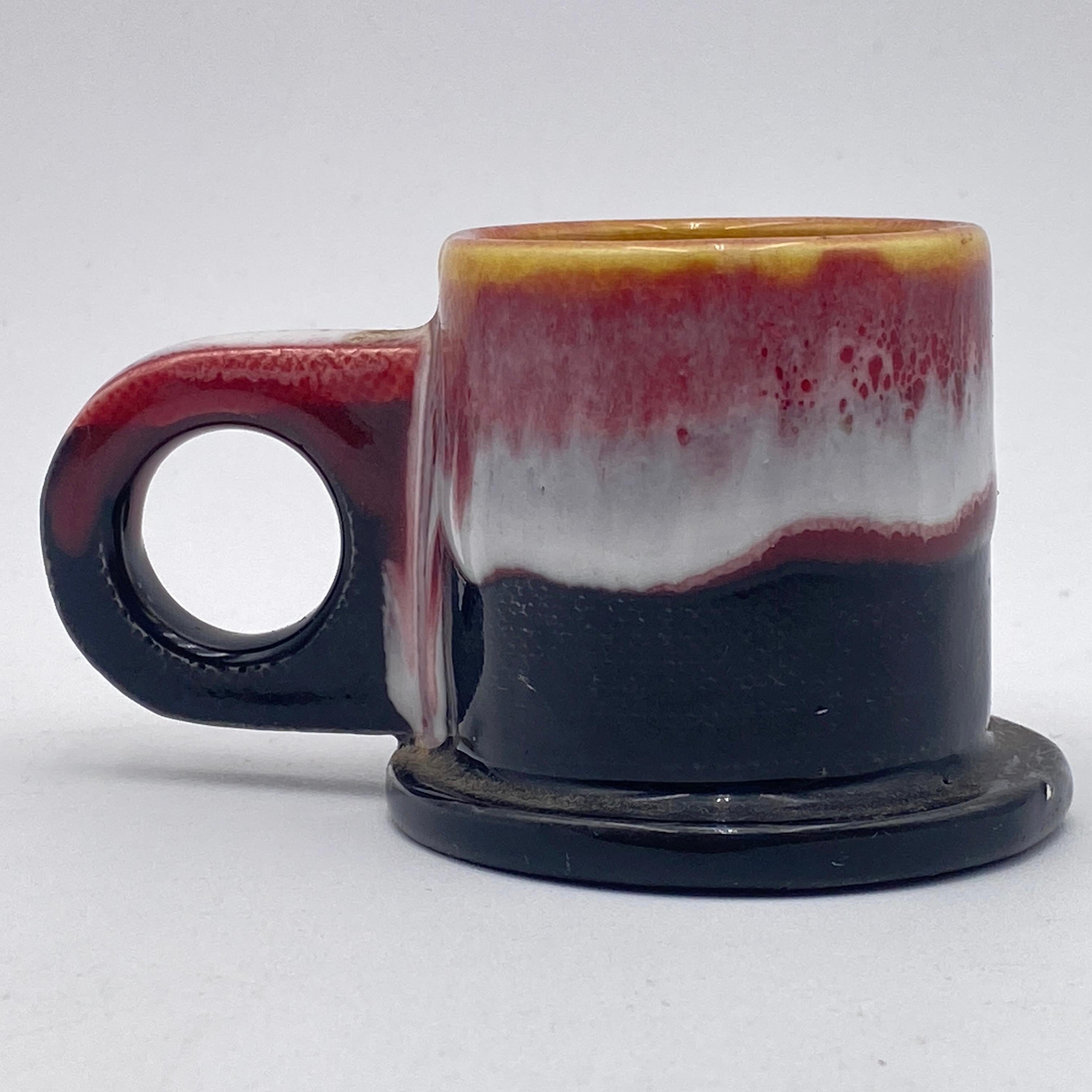 This is a set of two handmade ceramic espresso mugs with multicolored glaze by veteran Memphis artist Peter Shire. They are hand-painted, so no two are the same. At the base, each mug reads EXP 2013 in stamped relief text. 

Peter Shire is an