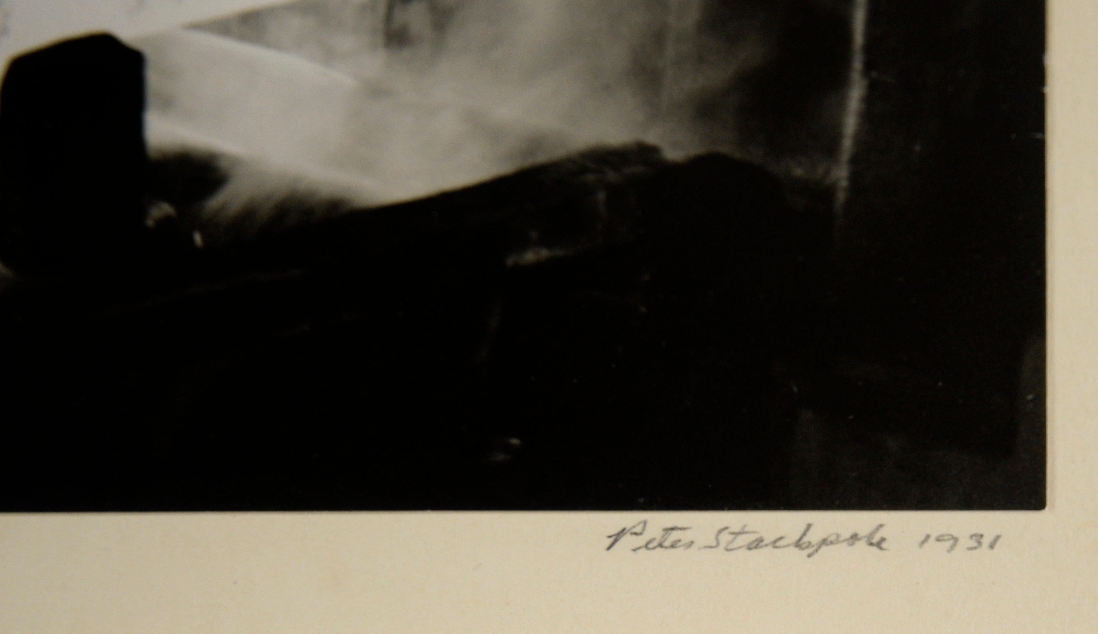 Kontrastreiches Foto von Peter Stackpole (Amerikaner, 1913-1997). Das Foto zeigt eine heiße Metallstange auf einer großen Maschine, die gerade bearbeitet wird. Das Metall glüht weißglühend und bildet einen starken Kontrast zum Rest der Fabrik und
