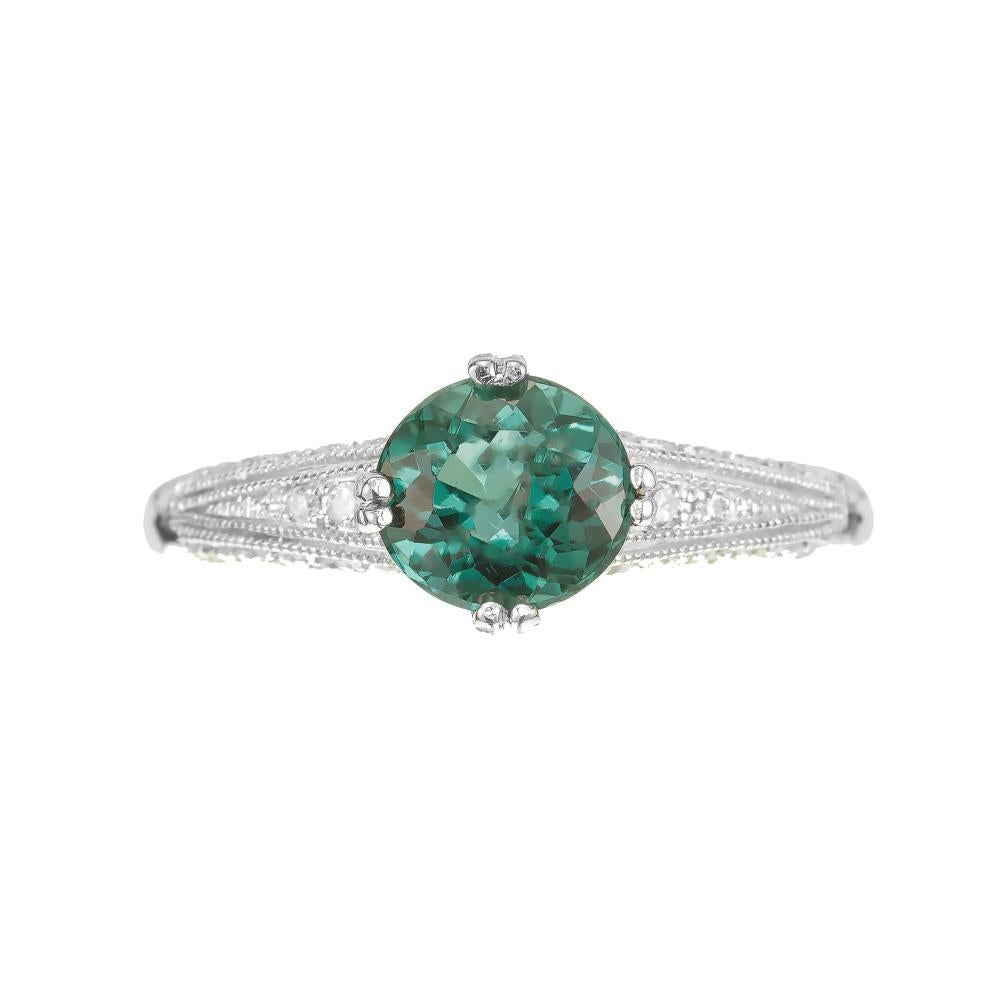 Tourmaline and diamond Art Deco inspired engagement ring. 1.23 carat bluish green round center tourmaline in an 18k white gold setting with 24 round cut accent diamonds. Designed and crafted in the Peter Suchy Workshop.

1 round bluish green