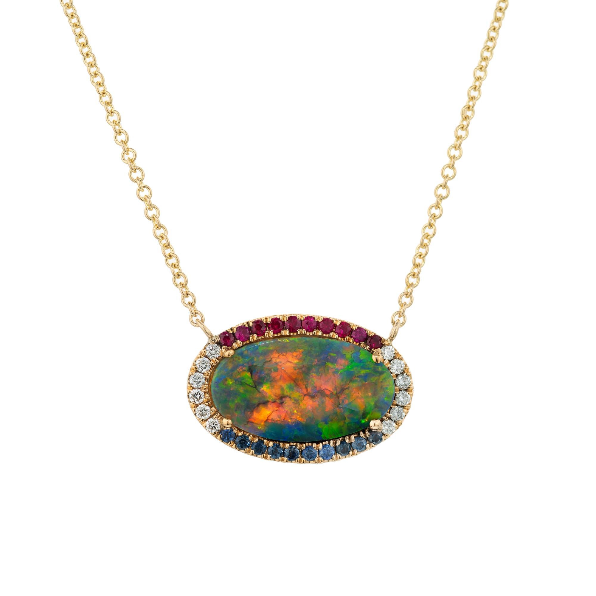 Opale australienne ovale extra fine de couleur rouge, verte et bleue montée dans une monture simple en or jaune 18 carats et rehaussée d'un halo de diamants ronds, de rubis et de saphirs. La chaîne fait 18 pouces de long. L'éclat chaud de l'or jaune