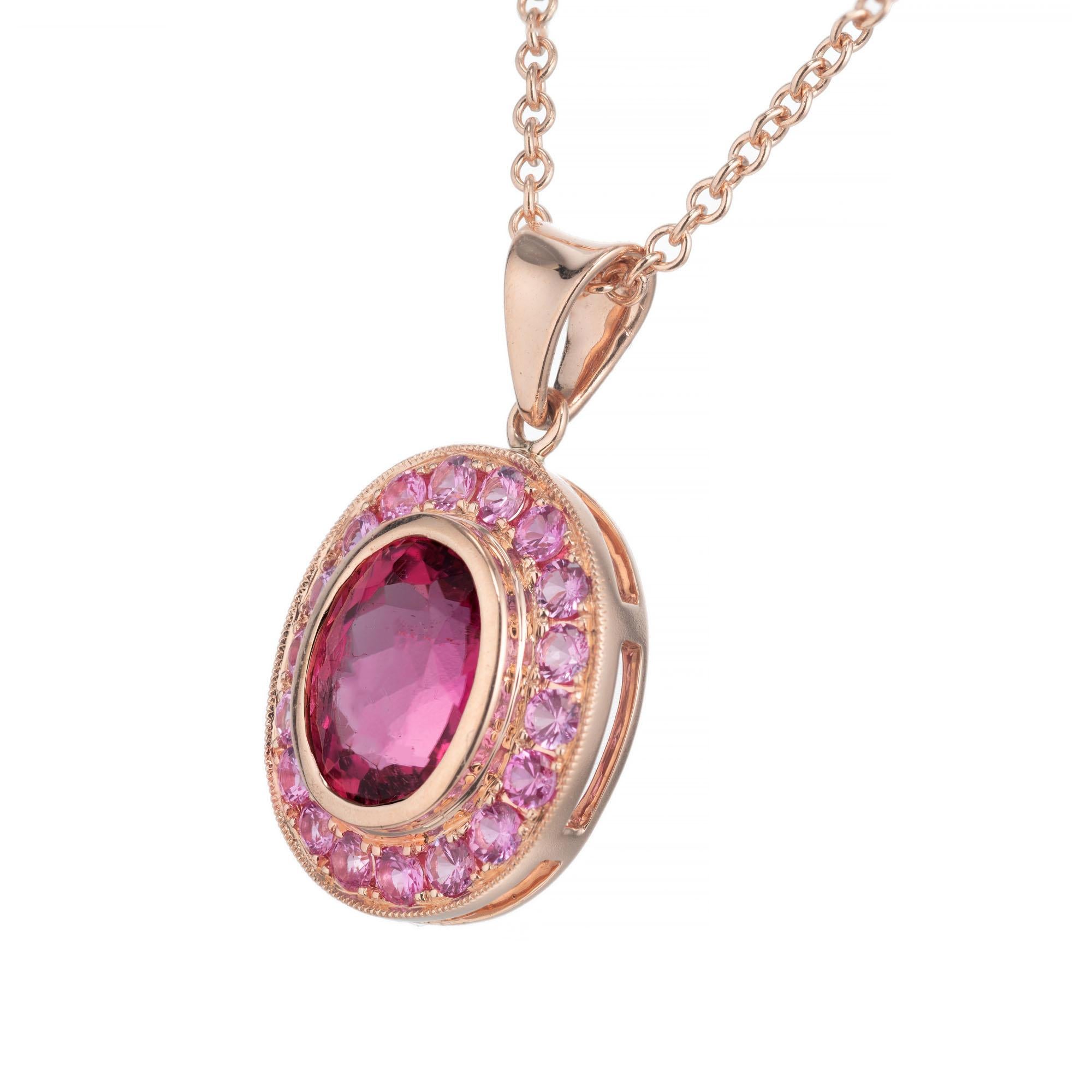 Oval pink tourmaline bezel set center stone with a halo of 18 round bead set pink sapphires, in 14k rose gold. 18 inch rose gold chain.  

 1 oval pink Tourmaline approx. total weight 2.15cts, 9.4 x 7.3mm. 
18 round pink sapphires approx. total