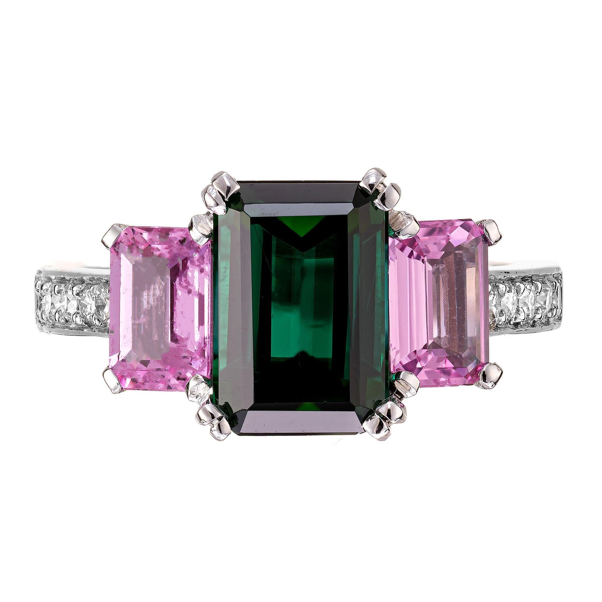 Tourmaline, sapphire and diamond engagement ring. Bright green emerald cut tourmaline center stone with 2 pink sapphire on each side in a three-stone platinum engagement setting, with pave diamonds along each side of the shank. Designed and crafted