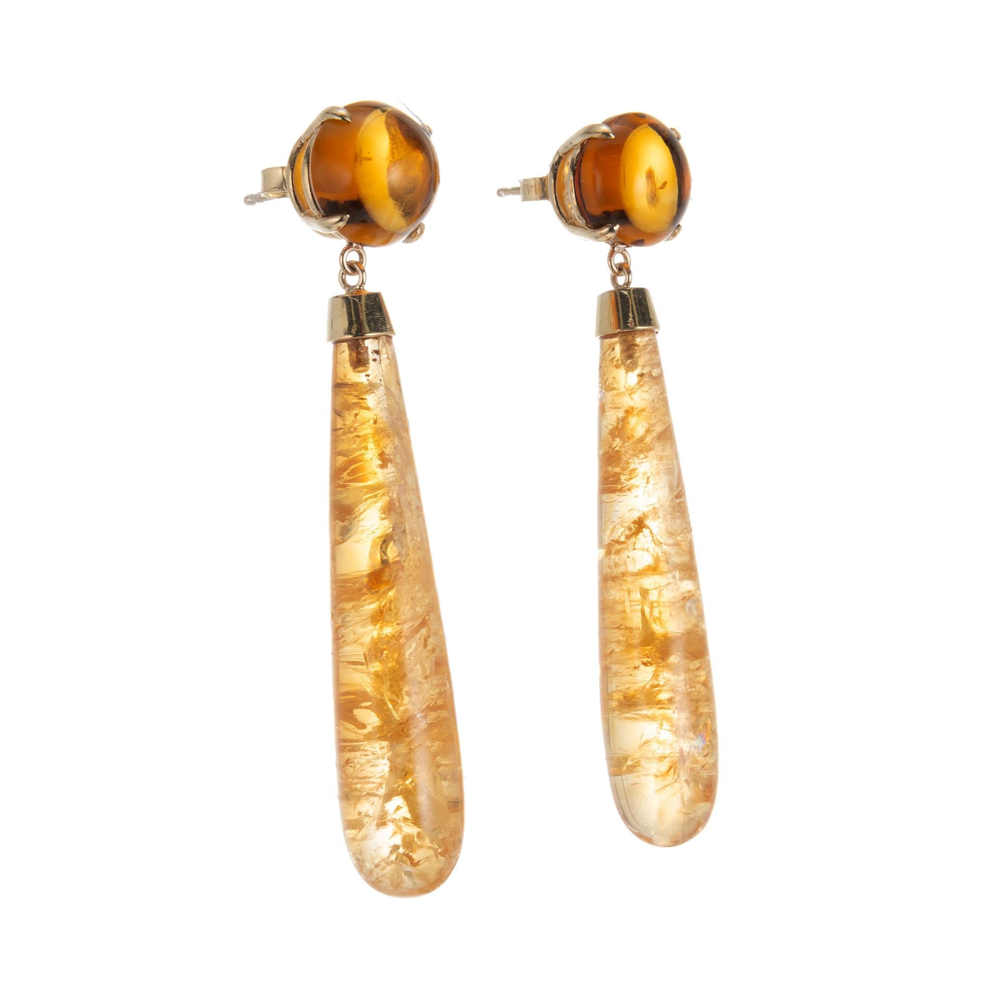Natural untreated citrine dangle earrings. Set in 14k yellow gold, two round citrine tops with two cylinder dangles. Made in the Peter Suchy workshop

2 cabochon mottled orange citrine cylinder, approx. 41.1cts
2 round cabochon brownish orange