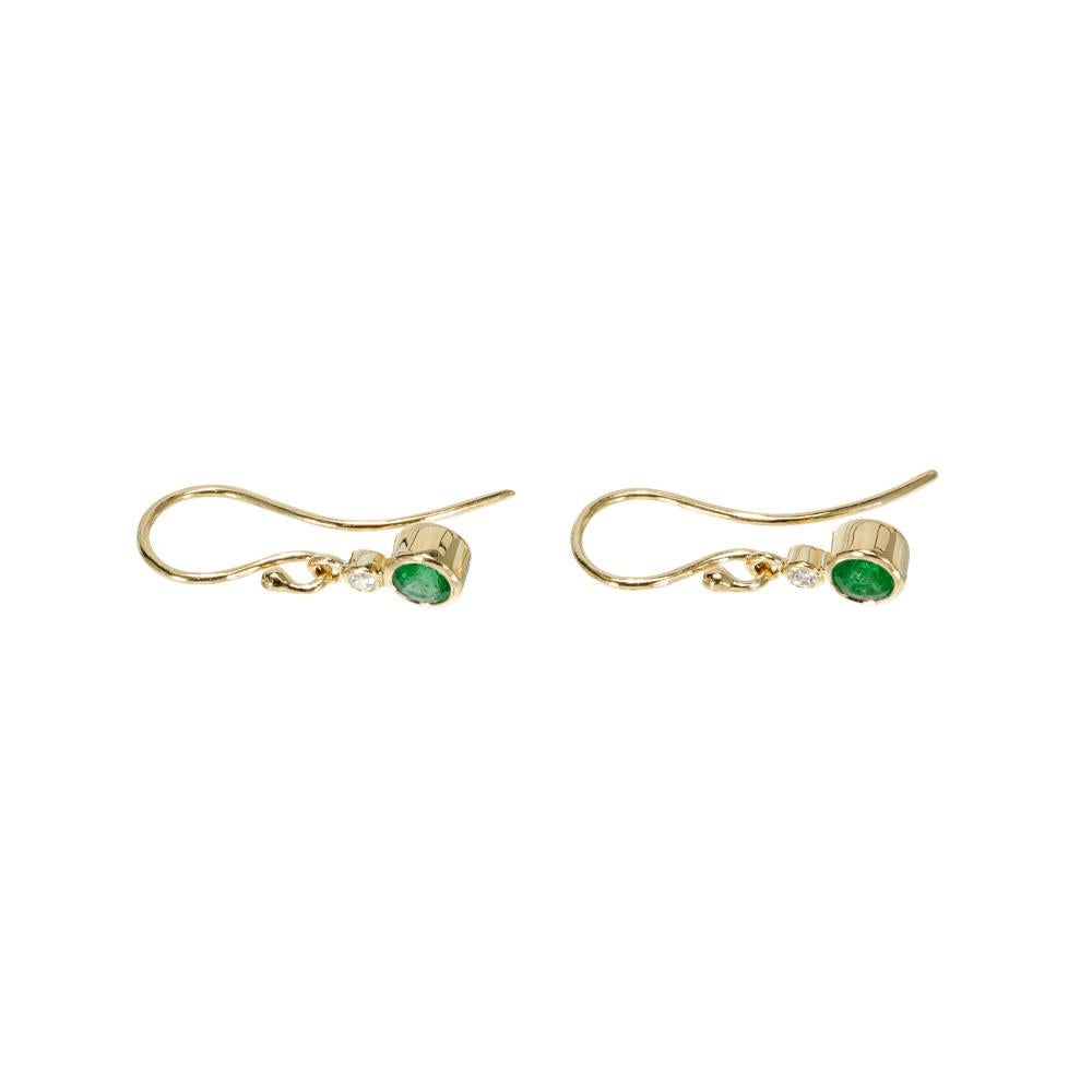 Boucles d'oreilles pendantes en émeraudes et diamants. 2 émeraudes rondes d'un vert riche et brillant montées sur un fil d'or jaune 18 carats en serti clos, accentuées par 2 diamants ronds en serti clos qui se trouvent juste au-dessus des émeraudes.