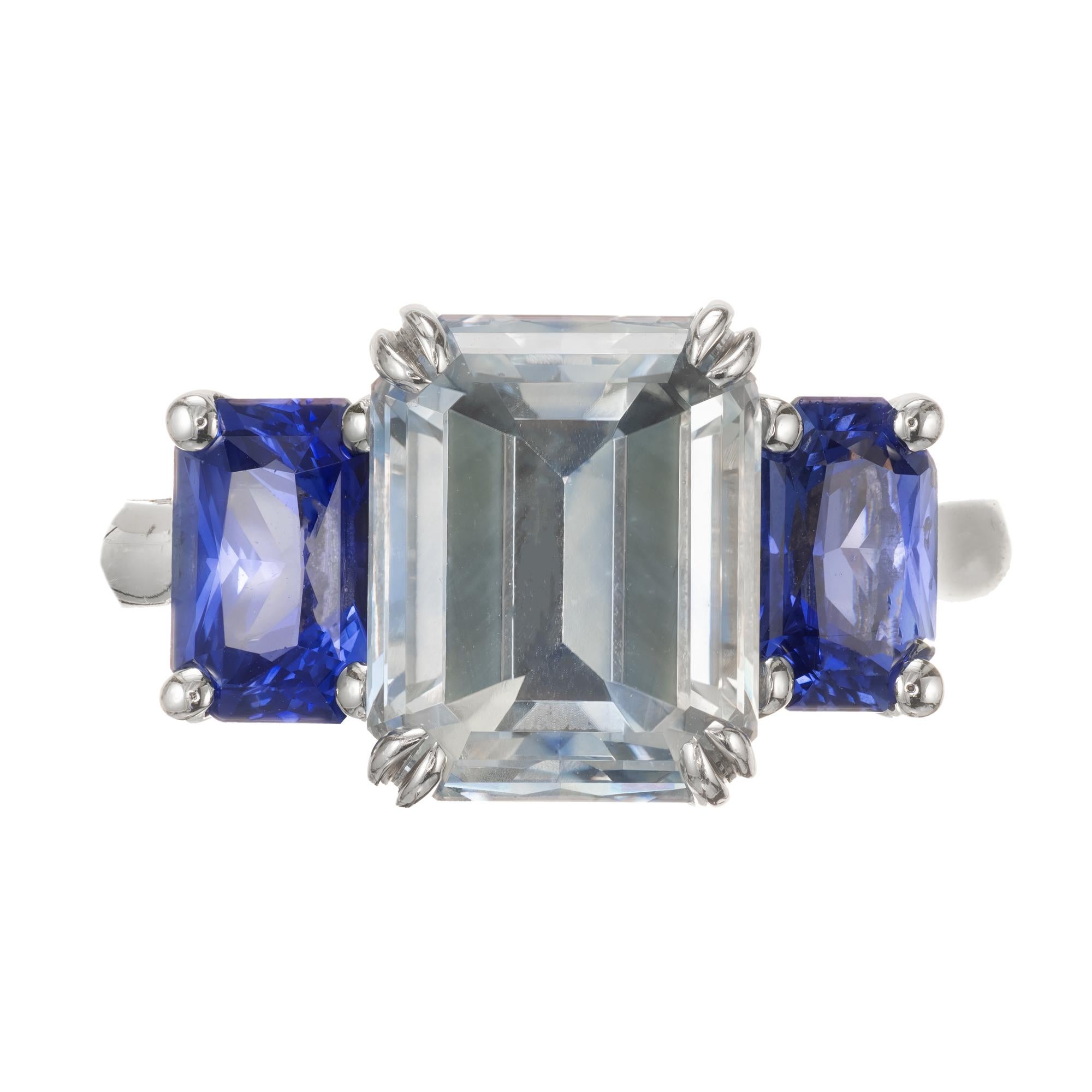 Natural AGL certified three-stone sapphire engagement ring. Emerald cut center sapphire sapphire,  AGL certified natural light gray blue white.  The light blue is a slightly purplish light blue, the gray cast is barely visible. There is some zoning
