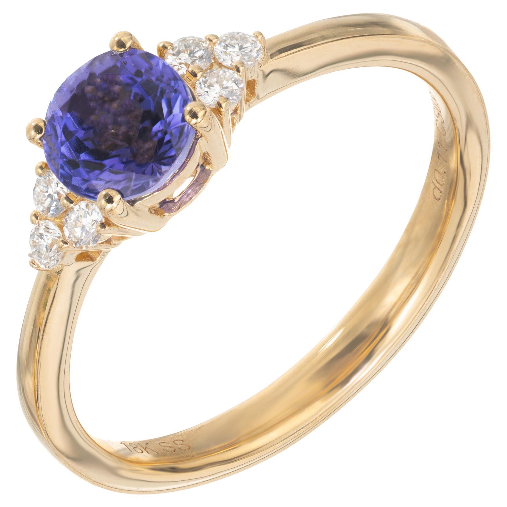 Tanzanite and diamond ring. Beautiful round cut purple and blue .88ct Tanzanite mounted in a simple four prong setting which is accented with 3 round brilliant cut diamond clusters on each shoulder. The setting is 18k yellow gold. Because of its